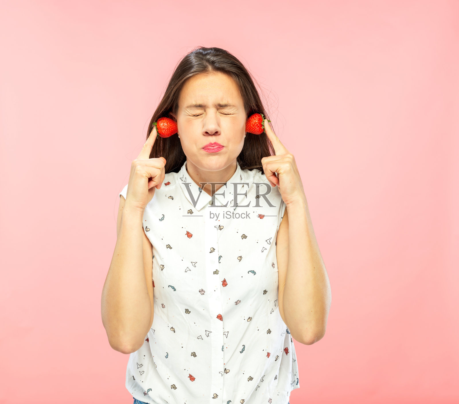 不高兴的年轻女人用草莓覆盖耳朵。照片摄影图片