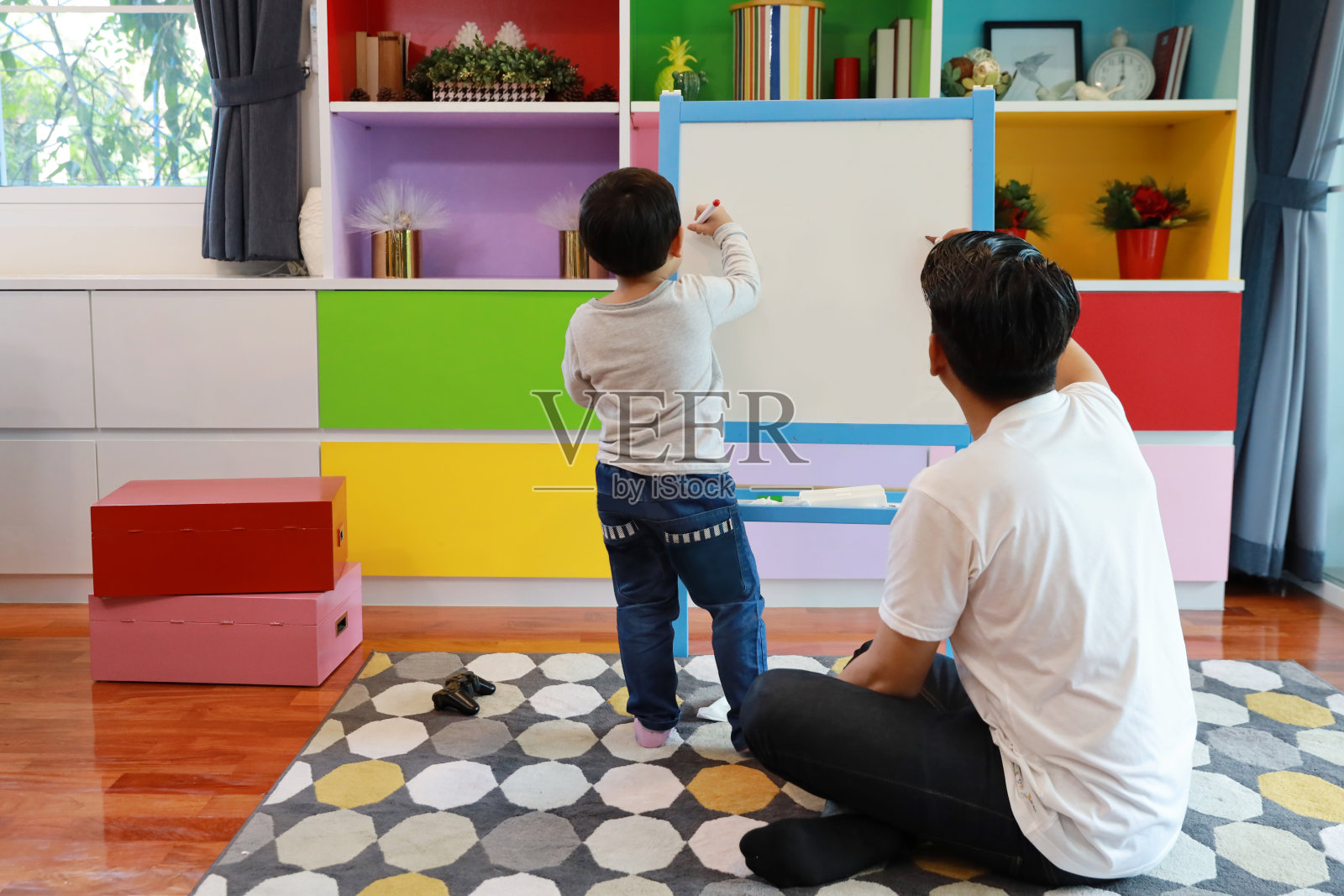 快乐的亚洲家庭单身爸爸带着快乐的笑脸在客厅的白板上教儿子画画(教育理念)照片摄影图片