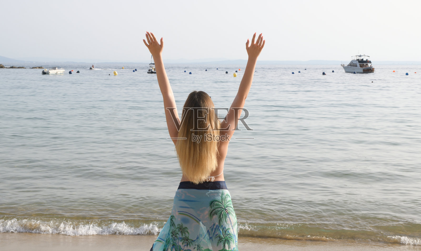 一个快乐的女人在海滩上举起手臂的背影肖像照片摄影图片
