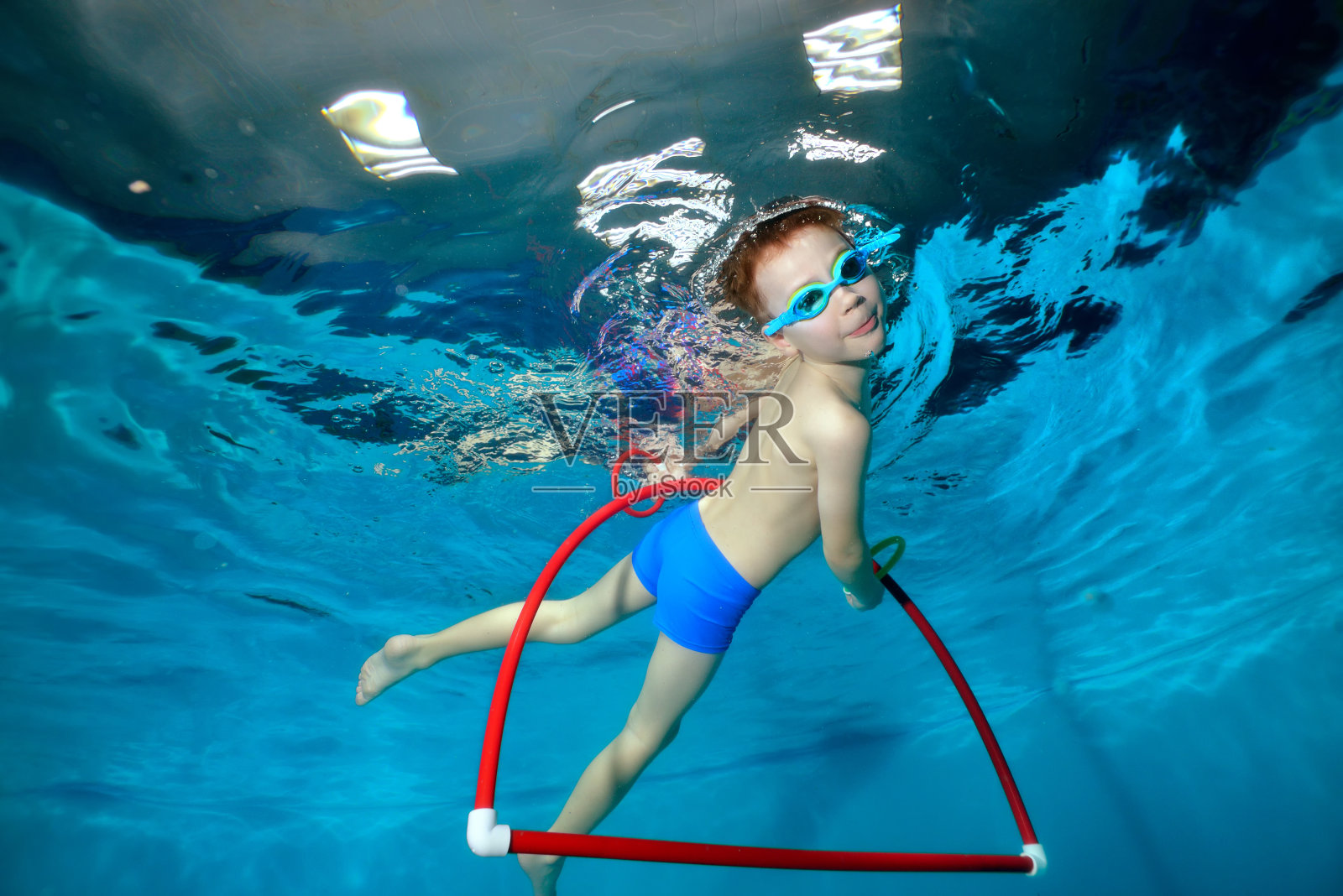 一个小体育男孩在泳池里游泳，浮出呼啦圈的水面，看着镜头。肖像。水下摄影。水平方向照片摄影图片