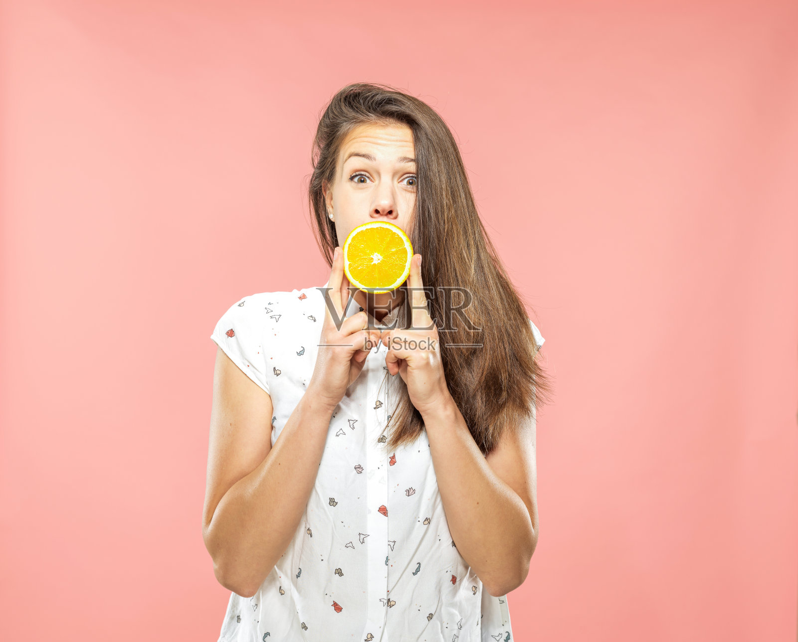 年轻的棕色头发的女人在敬畏覆盖嘴与一个橙色的一半照片摄影图片