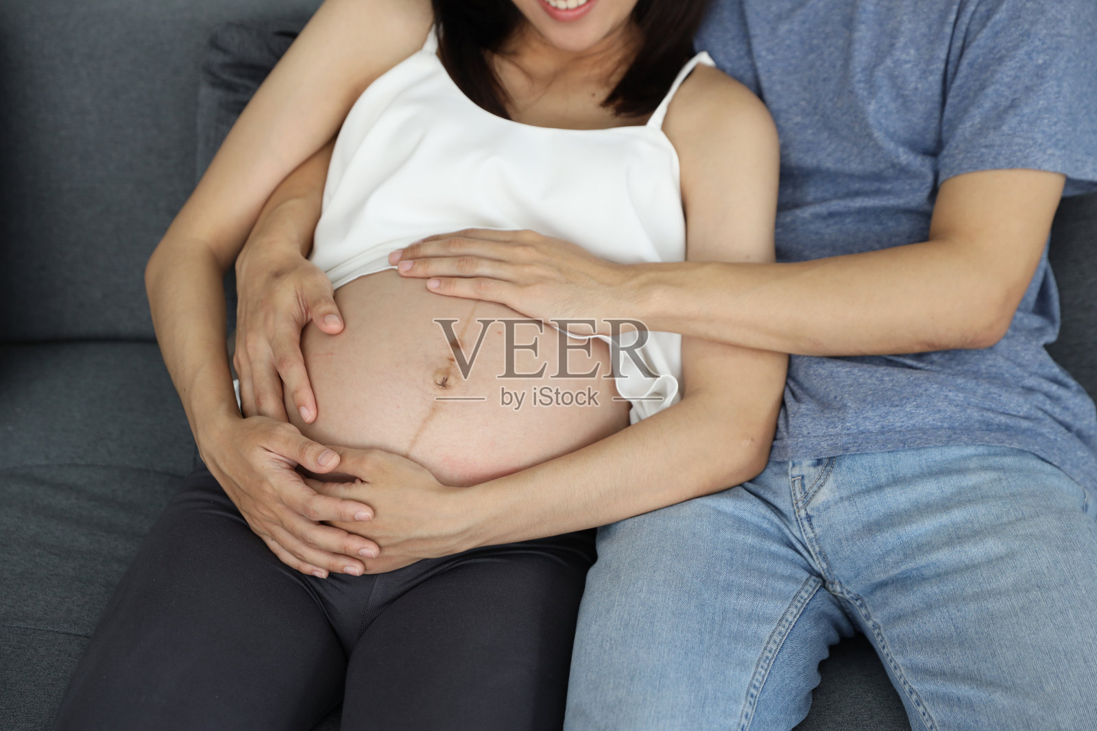 孕妇和丈夫在客厅沙发上满怀爱意地手牵着肚子照片摄影图片