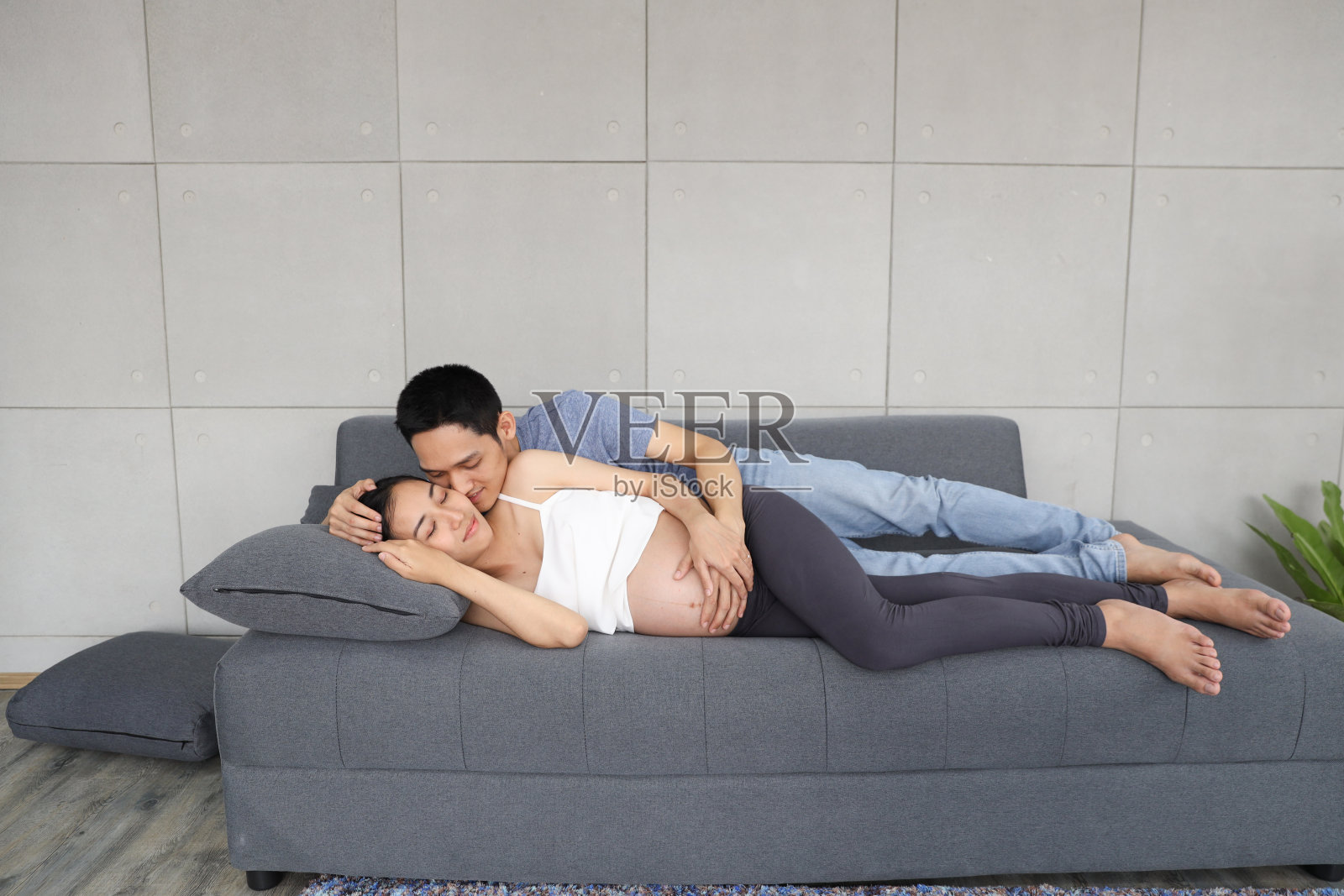 年轻亚洲夫妇在客厅沙发上拥抱亲吻孕妻照片摄影图片