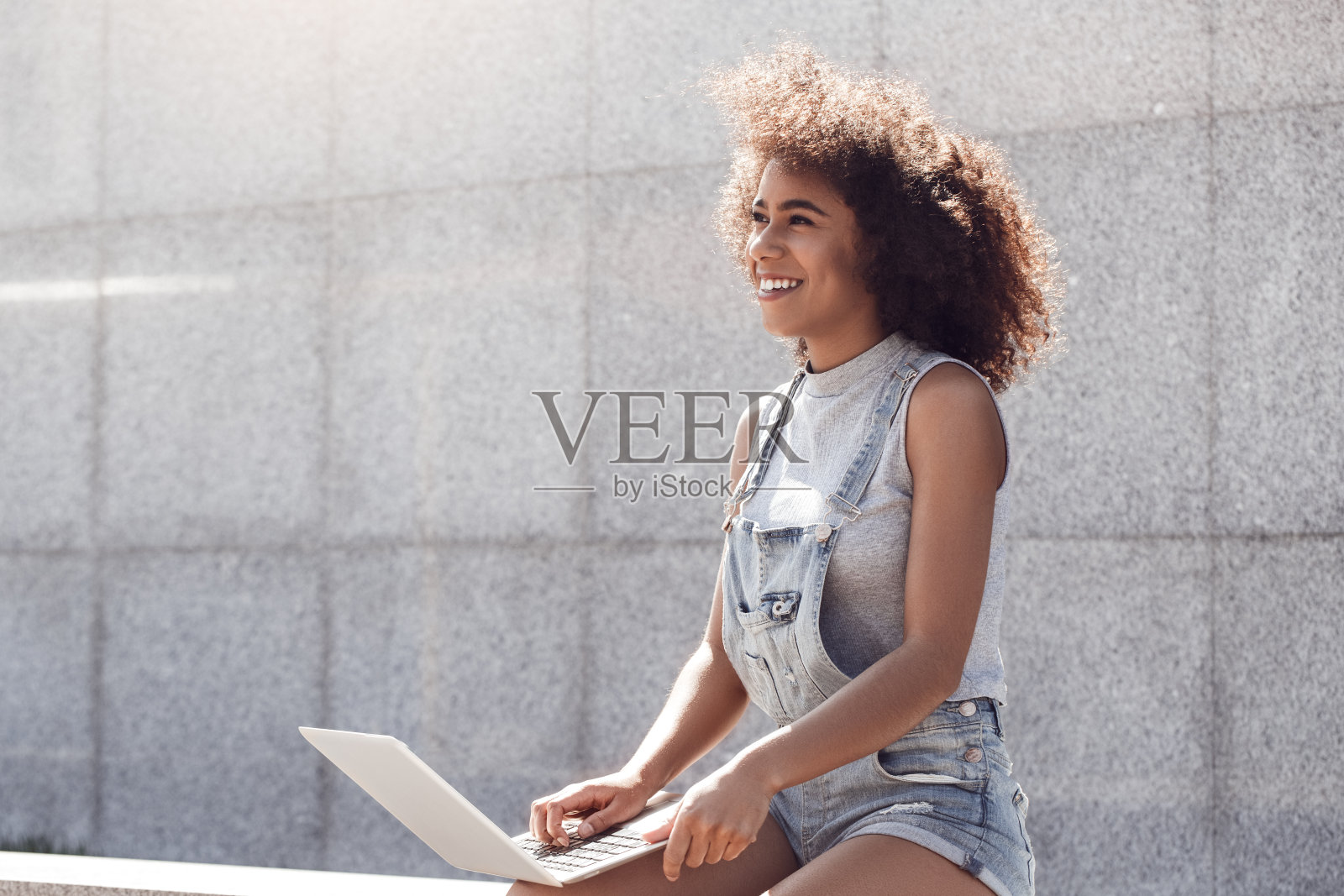 年轻女子穿着短裤坐在城市街道上，用笔记本电脑期待着快乐的梦想照片摄影图片