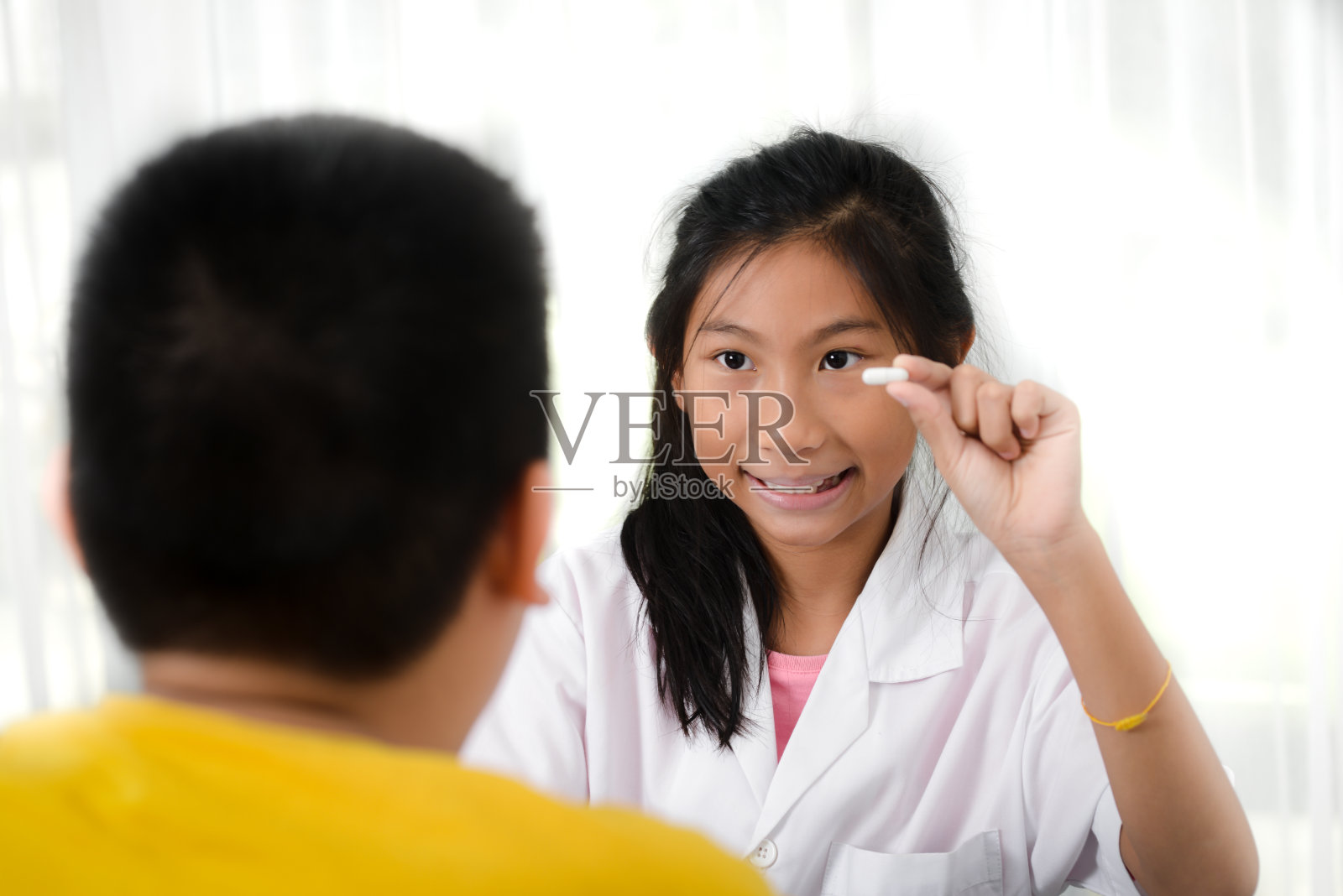 亚洲女孩药剂师向一个十来岁的男孩解释一些东西，拿着用药片起的水泡，保健概念。照片摄影图片