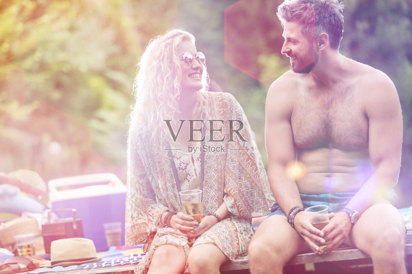 微笑的年轻金发女人和赤膊胡子男人坐在码头上喝着饮料照片摄影图片