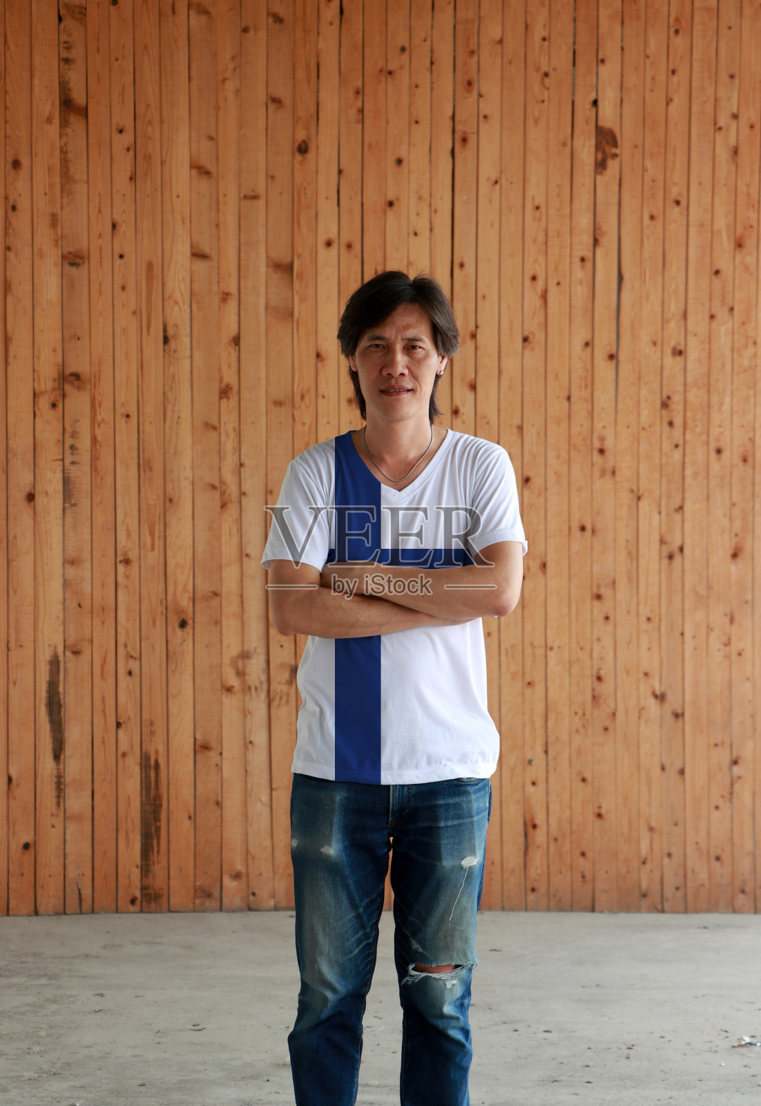 男子穿着芬兰国旗颜色的衬衫和交叉手臂在木墙背景。照片摄影图片