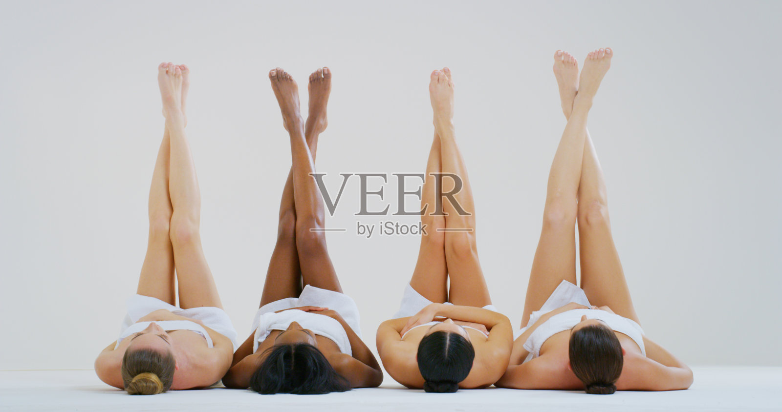 不同种族的美丽年轻女性的肖像，完美的坚定和苗条的身体，无毛的柔软和丝绸般的双腿交叉孤立在一个白色的背景。照片摄影图片