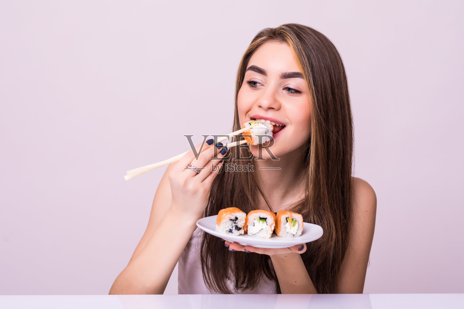 年轻漂亮的女人用筷子吃寿司，孤立在白色的背景照片摄影图片