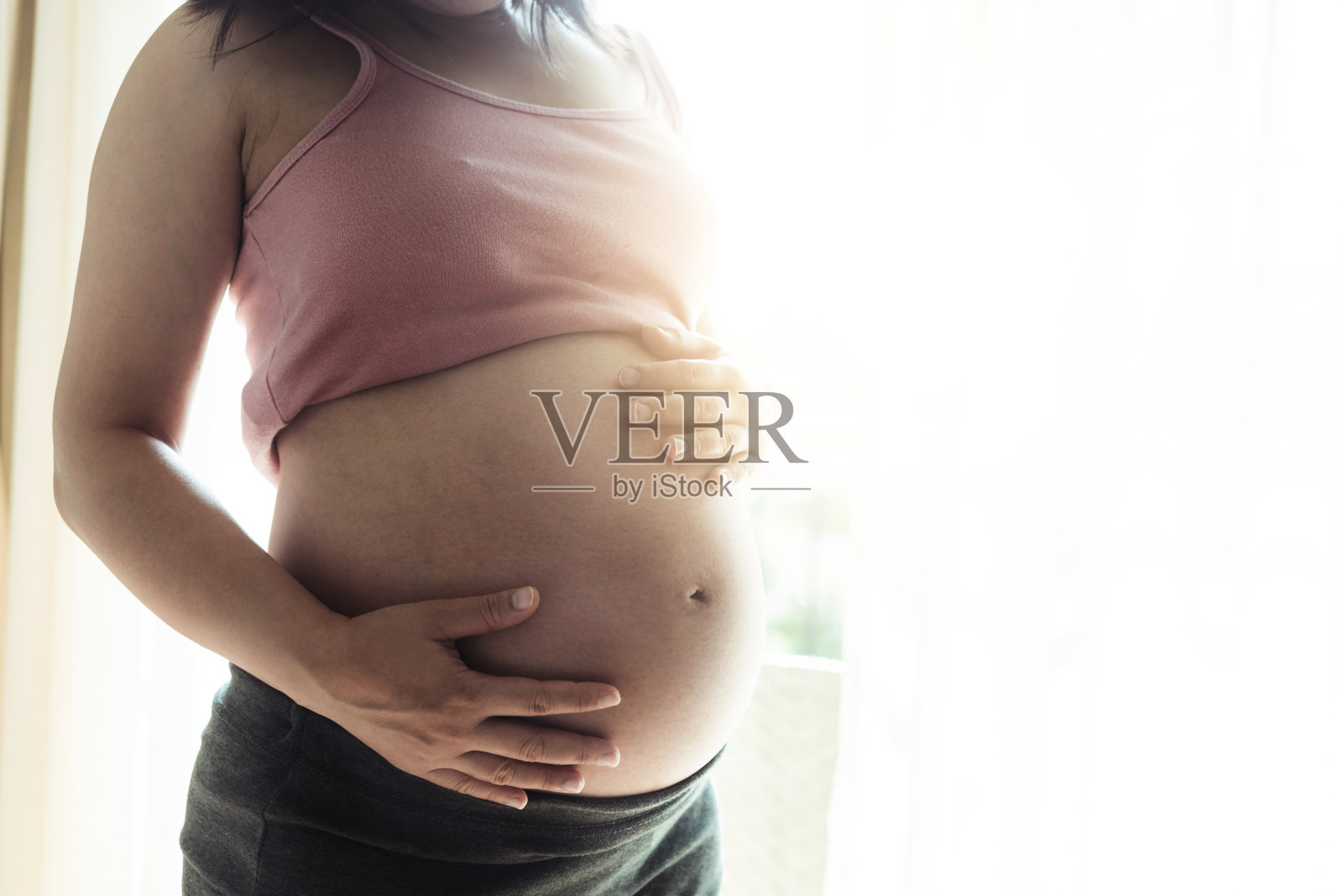 孕妇在家照顾孩子时感到快乐。年轻的孕妇抱着怀孕的肚子里的婴儿。孕产妇产前护理与妇女怀孕的概念。照片摄影图片