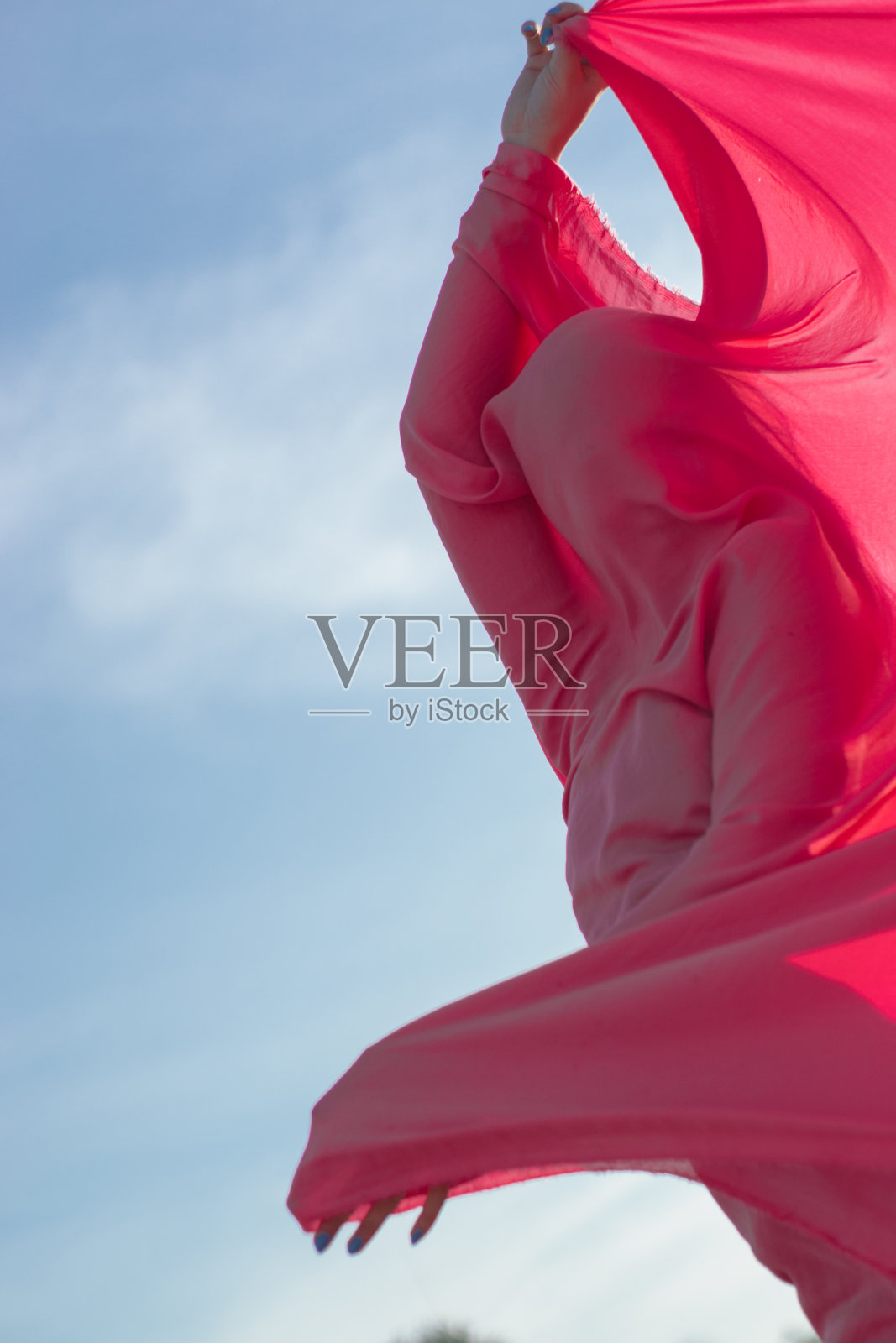 粉红色头发的年轻女子用粉红色的布片和风力发电机在田地附近跳舞。风车在日落。时尚的肖像照片摄影图片