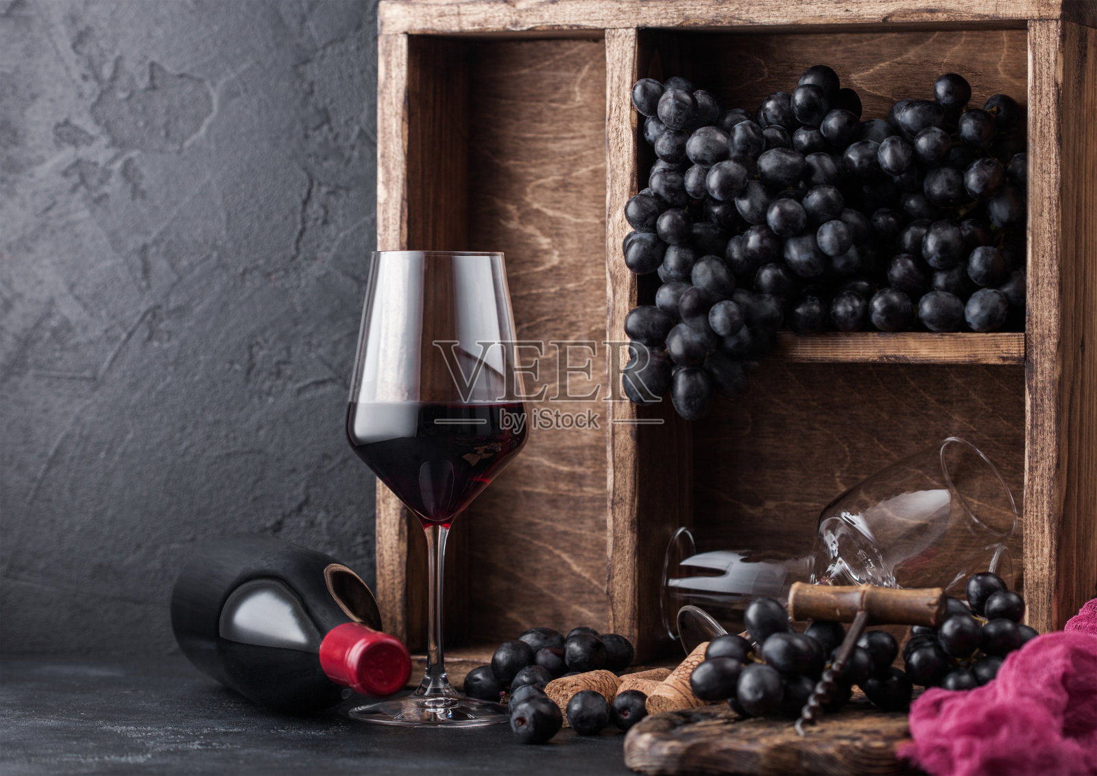 葡萄酒与黑葡萄在vintage木盒黑色的石头背景。优雅的葡萄酒杯与软木塞和螺旋塞在黑板上。自然光线照片摄影图片