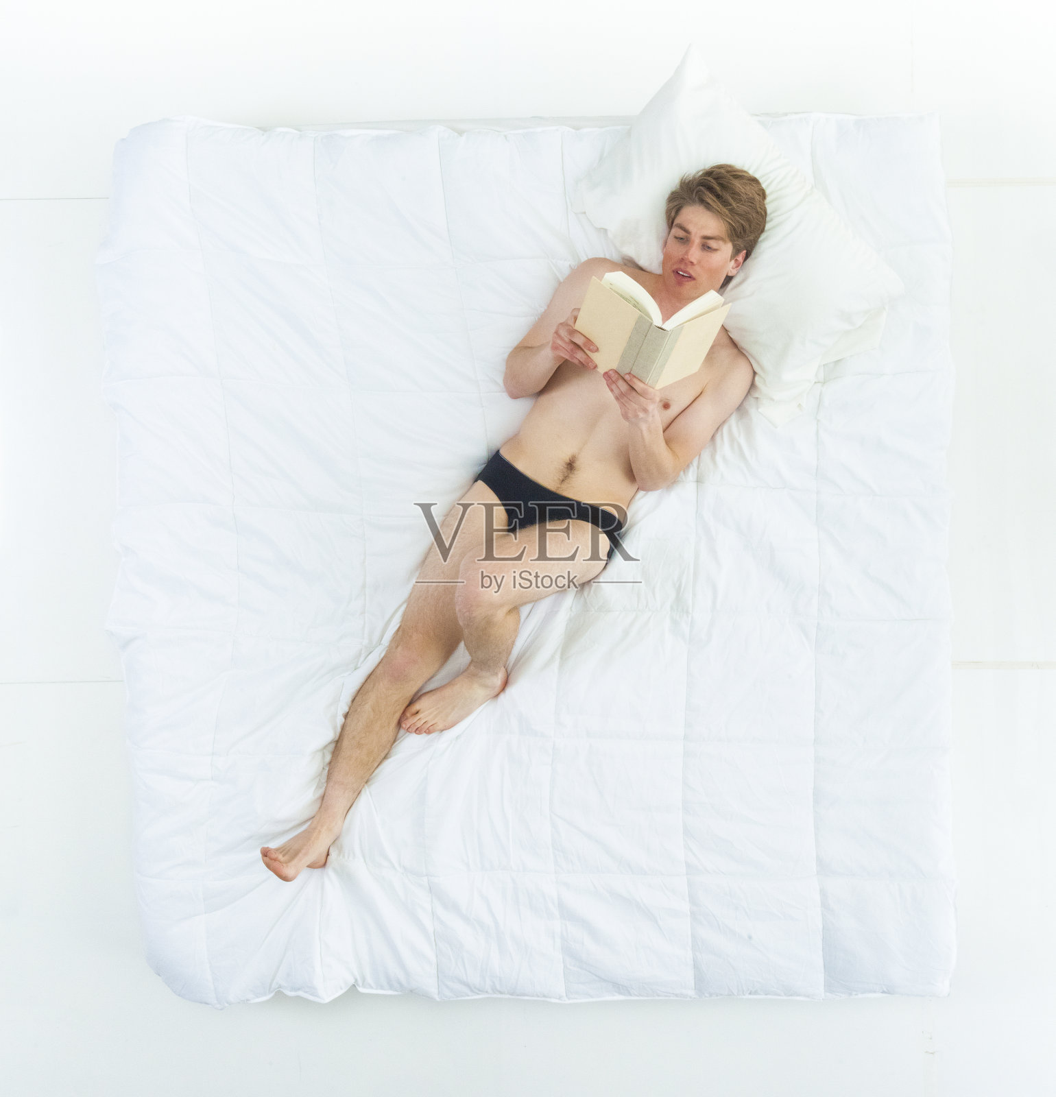 性感的男人在床上穿着内衣，看书照片摄影图片