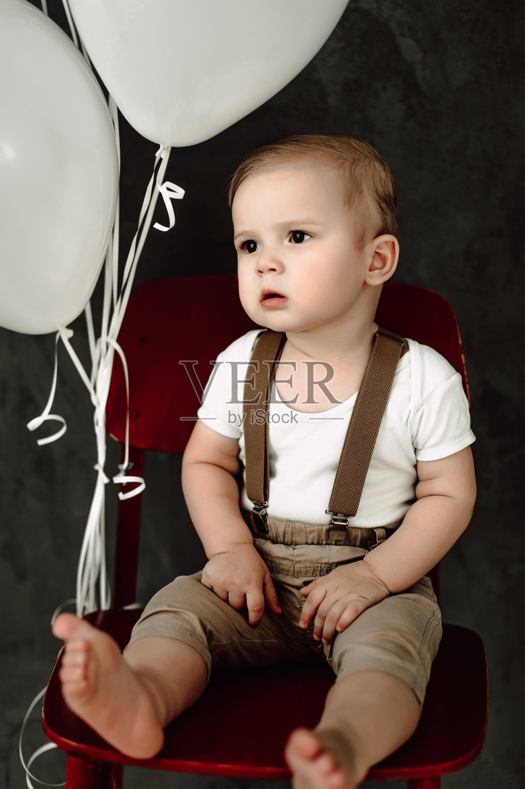 可爱的小男孩开心的微笑庆祝一岁生日的肖像。一岁的欧洲小绅士坐在椅子上玩气球照片摄影图片