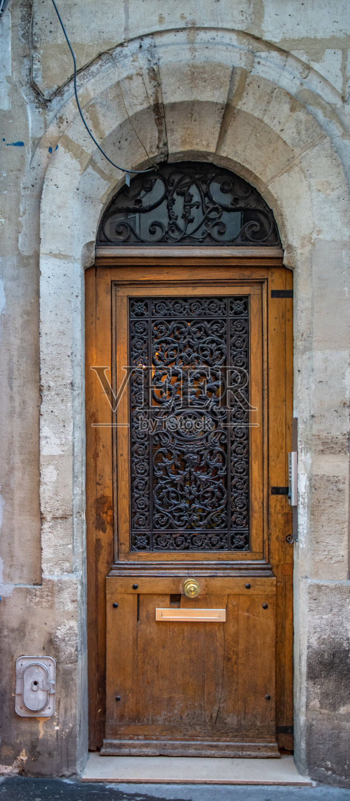 法国巴黎古老建筑石拱下的带有装饰金属网格的老木门。法国街头古色古香的古色古香的木门和久经风蚀的灰色石墙。照片摄影图片