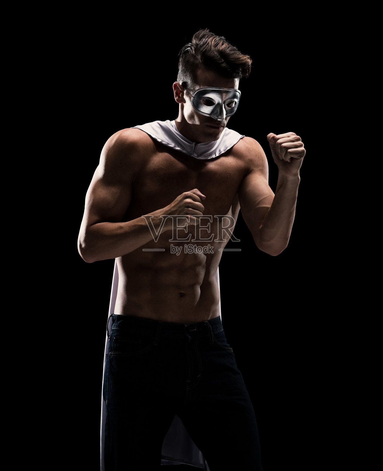 性感的男性超级英雄在黑色背景下戴着面具，斗篷和牛仔裤照片摄影图片