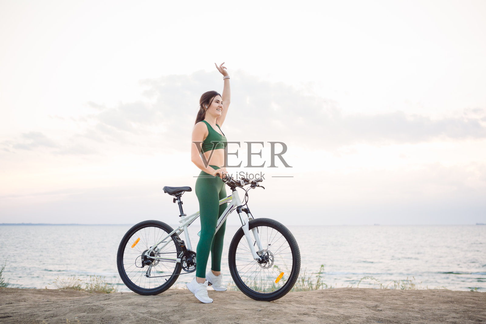 日出时分骑着自行车的年轻褐发女人。照片摄影图片