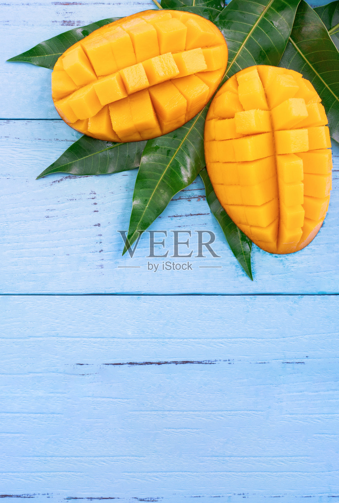 鲜切芒果与绿色叶片，明亮的蓝色木材背景。上方视图，平铺，复制空间，关闭。热带水果的概念。照片摄影图片