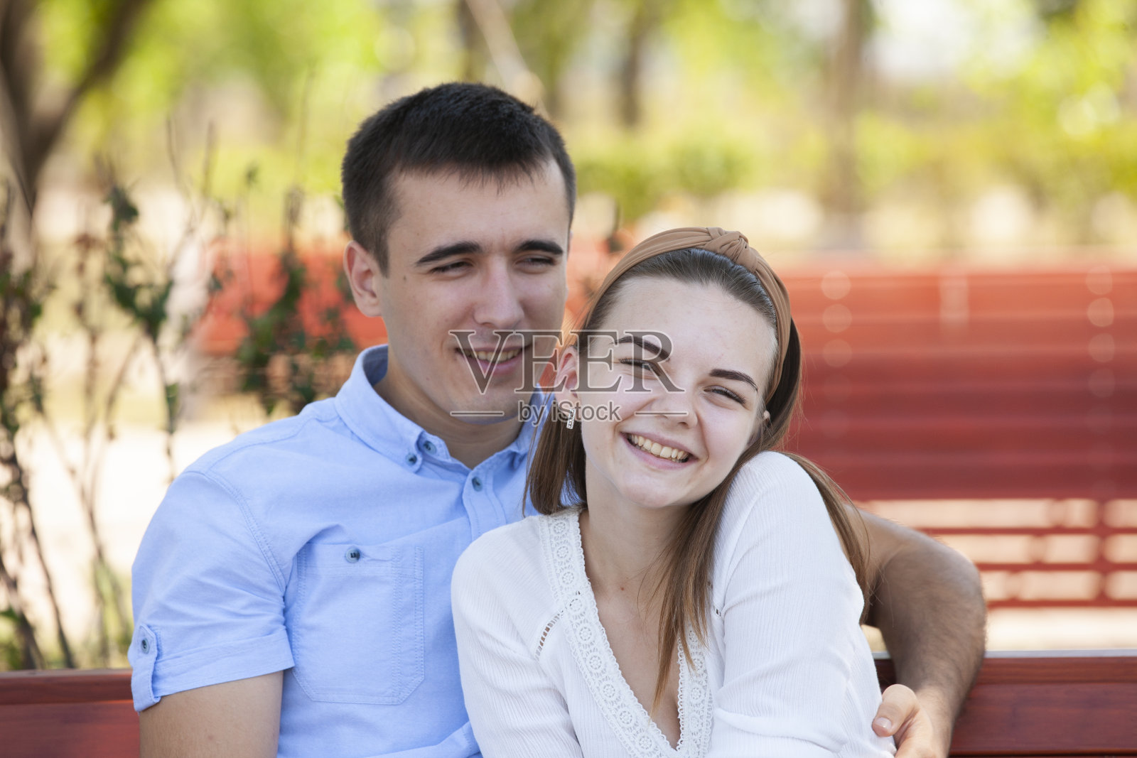 一对年轻夫妇坐在公园的长椅上。照片摄影图片