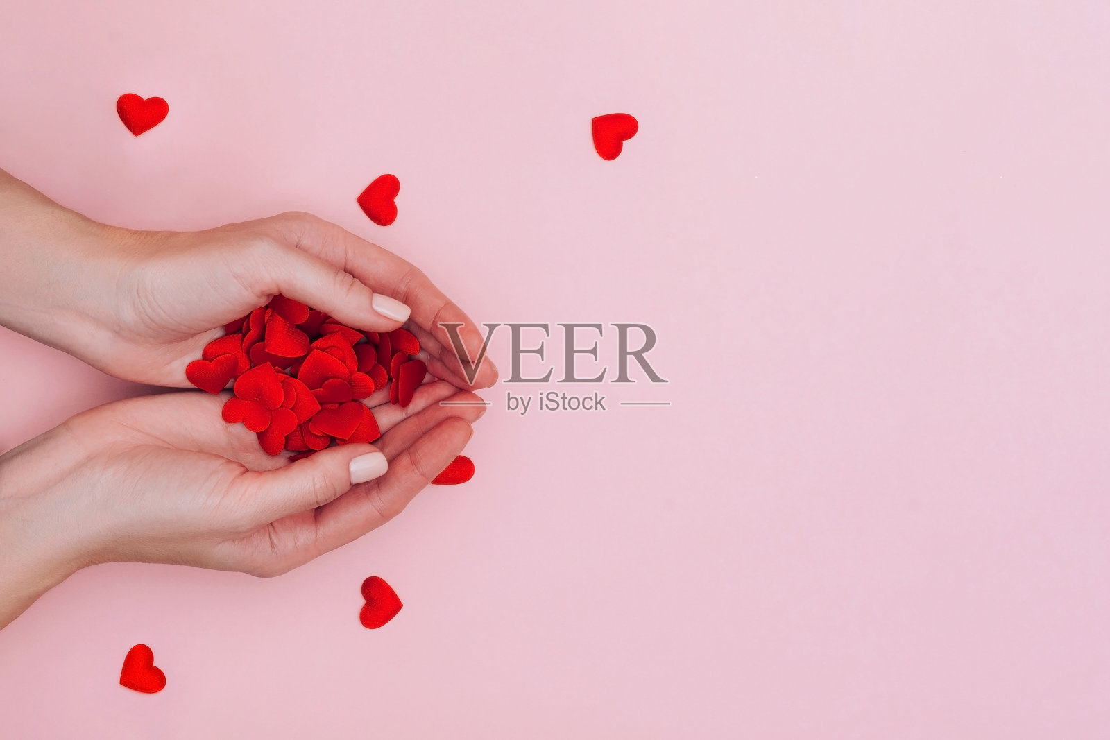 女人的手满是粉红色背景上的小红心。爱情、关怀、亲情、情人节的概念。照片摄影图片
