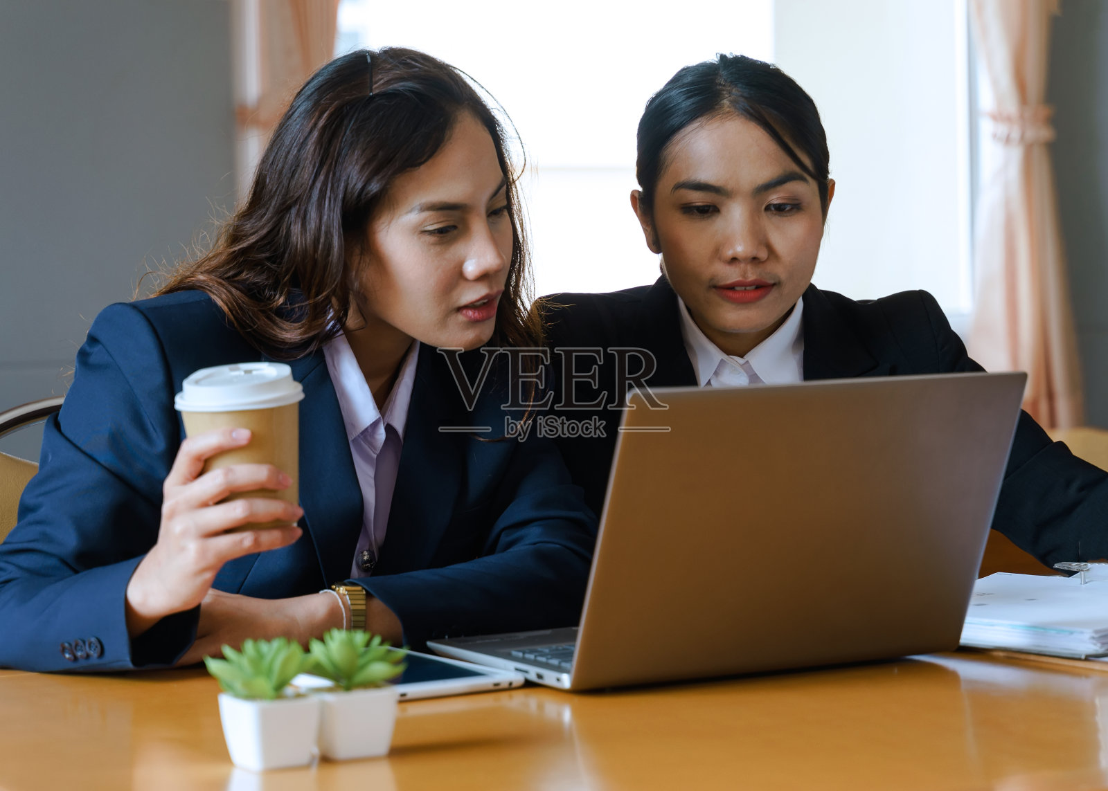 两个年轻的商业女性在现代办公空间讨论商业项目。两个女办公室工作人员穿着商务套装一起工作在现代办公室的新项目。女人在一起工作。照片摄影图片