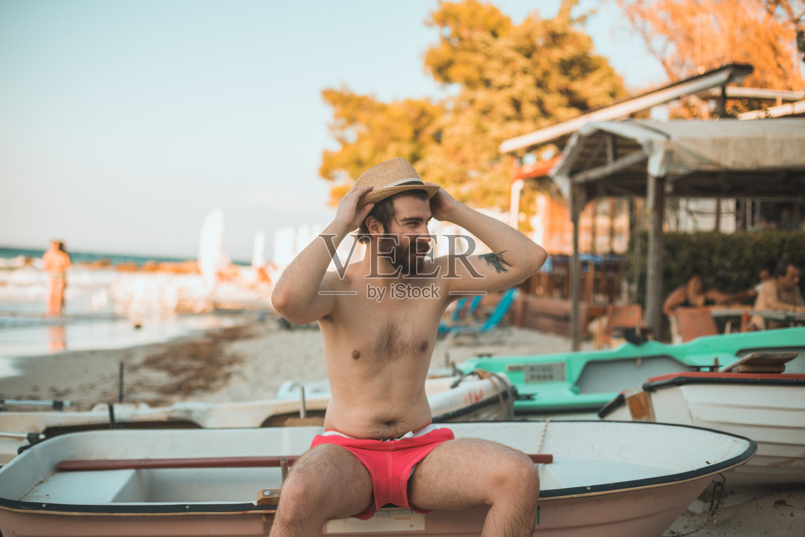 英俊的男人坐在海边的小船上照片摄影图片