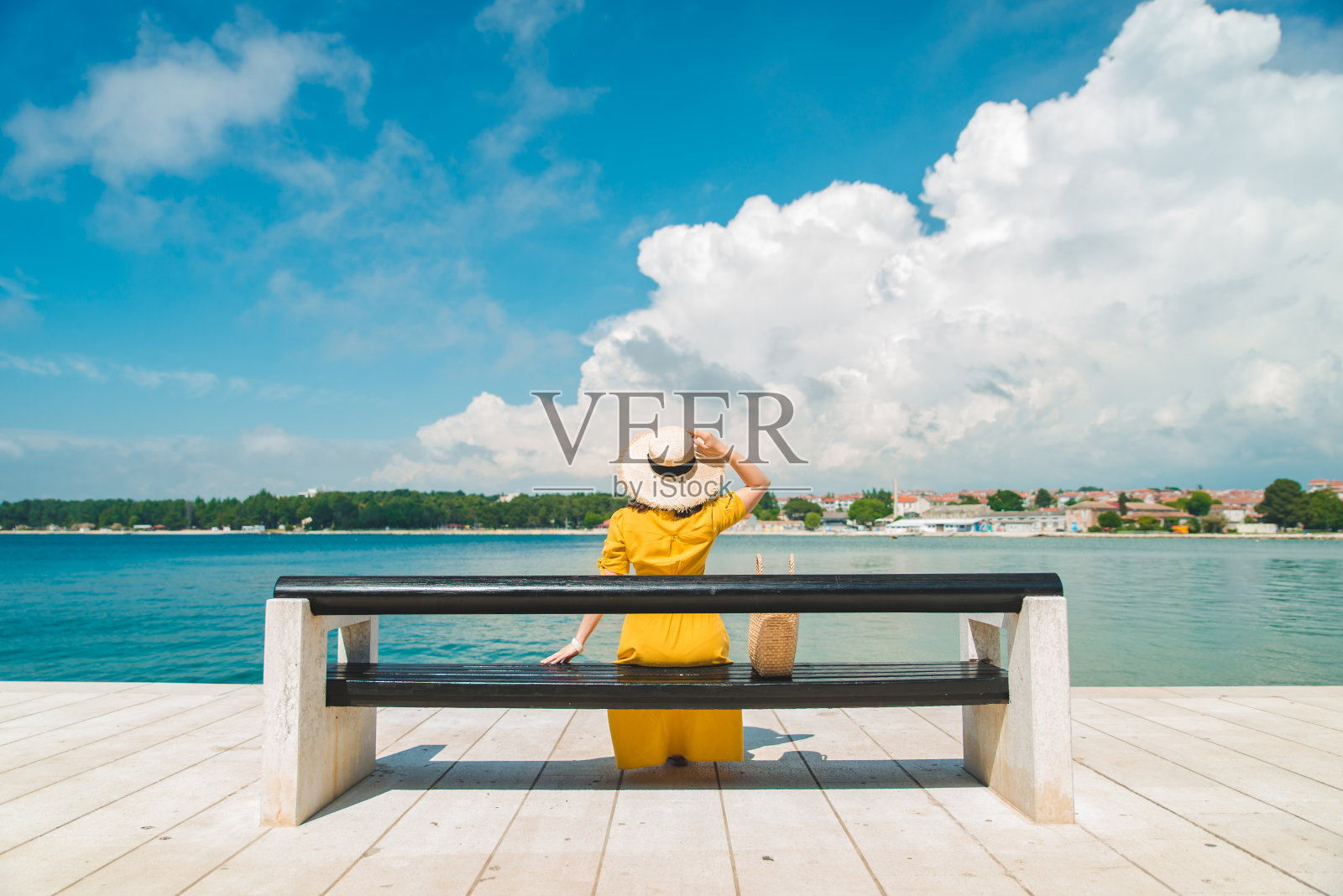 一个女人坐在长椅上，穿着黄色背心裙，欣赏着海景照片摄影图片