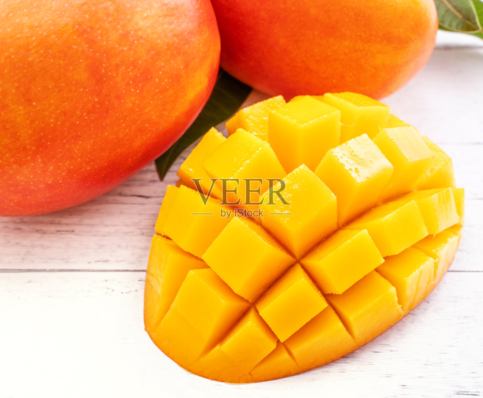 美丽的切碎的芒果与绿色的叶子在明亮的白色木材背景。上方视图，平铺，复制空间，关闭。热带水果的概念。照片摄影图片