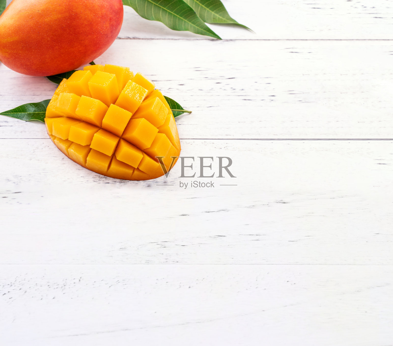 美丽的切碎的芒果与绿色的叶子在明亮的白色木材背景。上方视图，平铺，复制空间，关闭。热带水果的概念。照片摄影图片