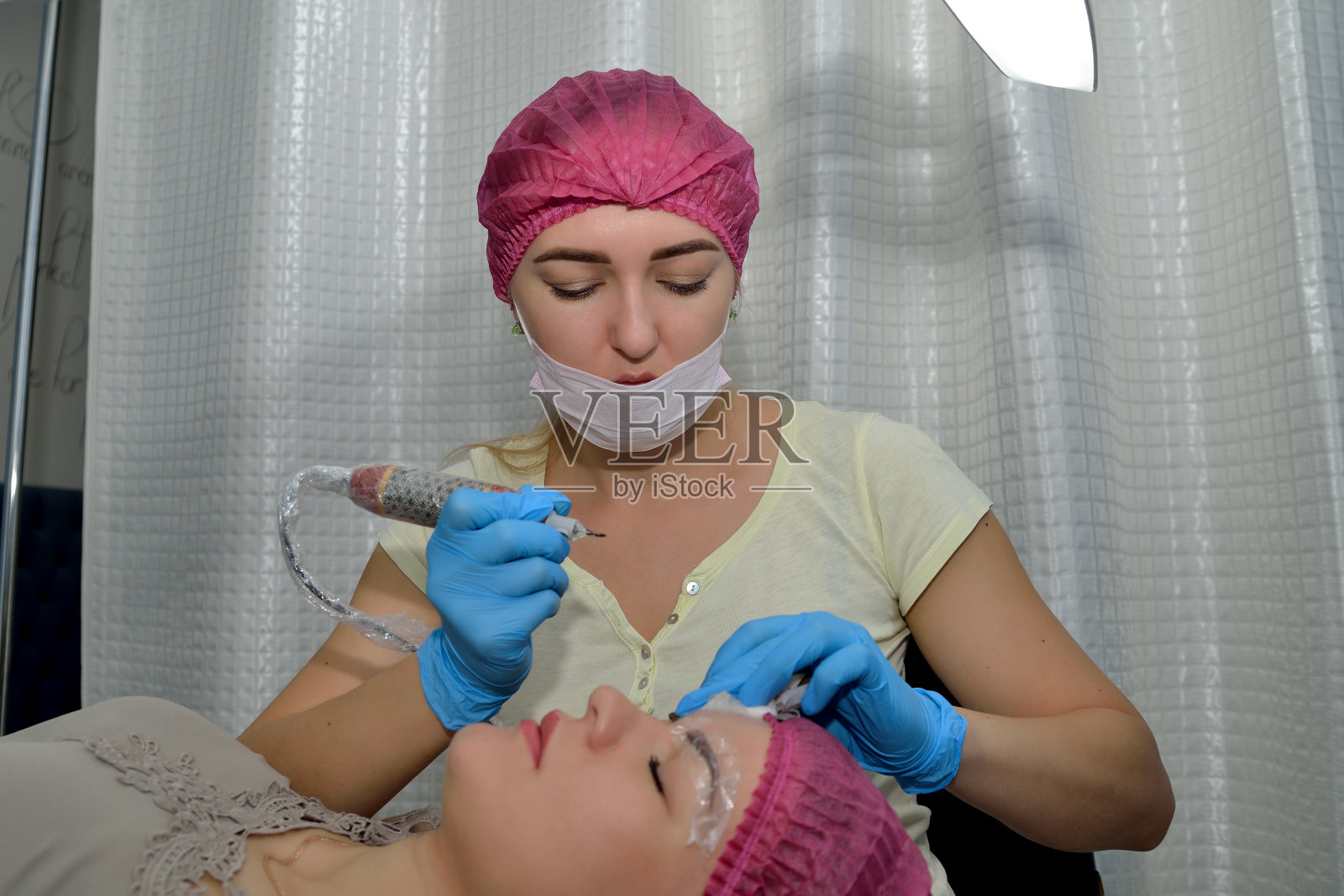 眉microblading过程。美容师用美容工具使病人俯身。关闭了。横向视图照片摄影图片