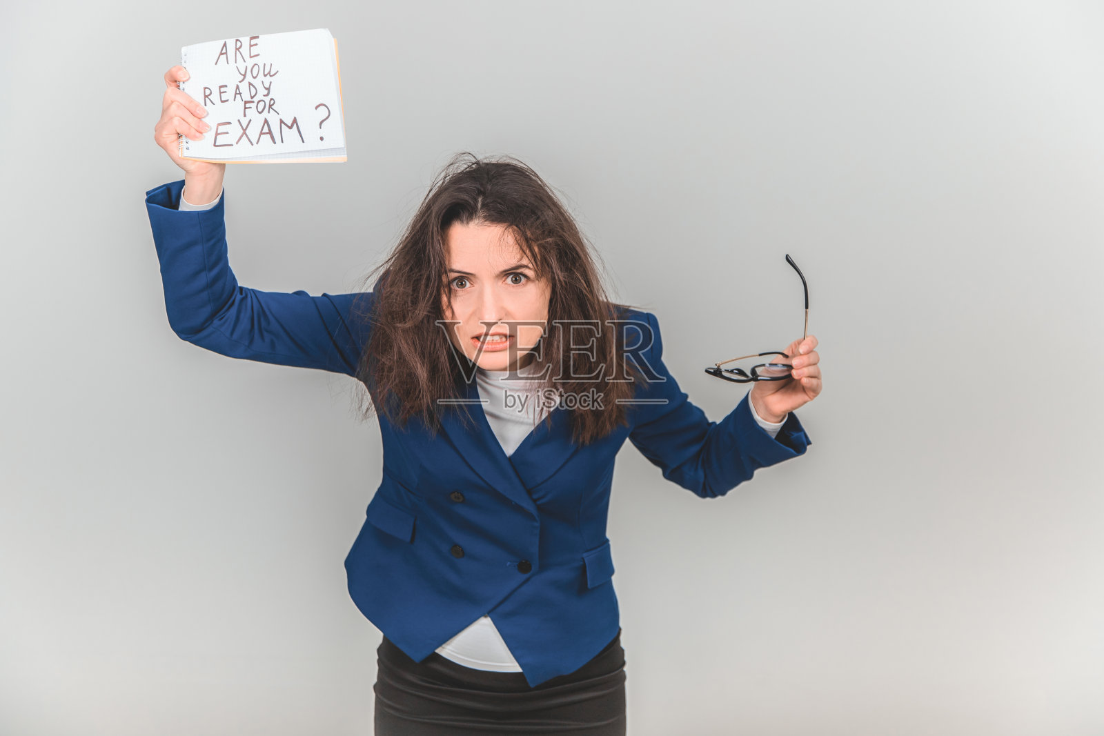 疲惫不堪的年轻老师站在那里，手里拿着一张写着准备考试的纸条。她头发蓬乱，咬紧牙关，看起来很疯狂。照片摄影图片