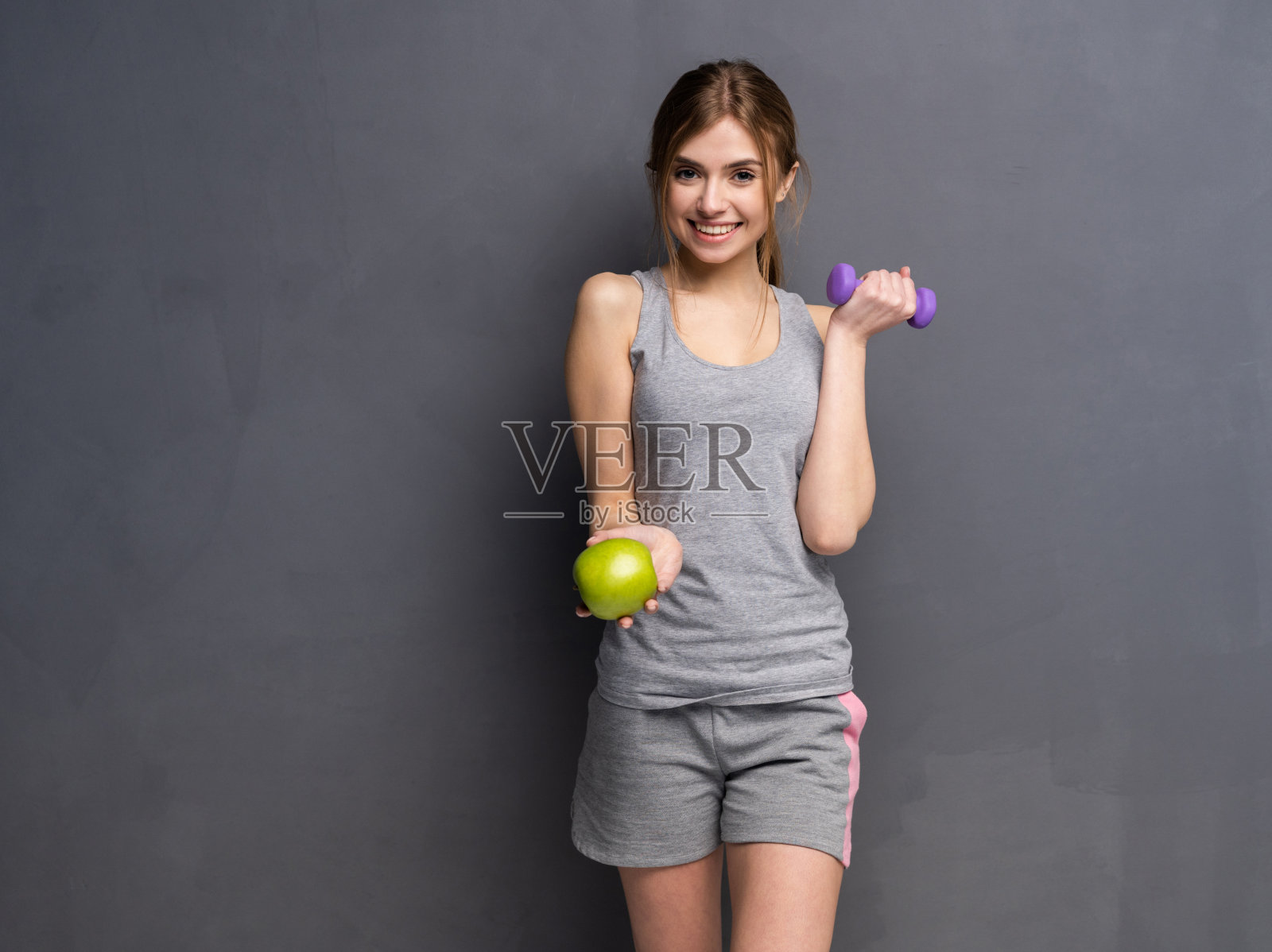 运动健将举着哑铃，另一只手拿着苹果。健身与健康节食理念。照片摄影图片