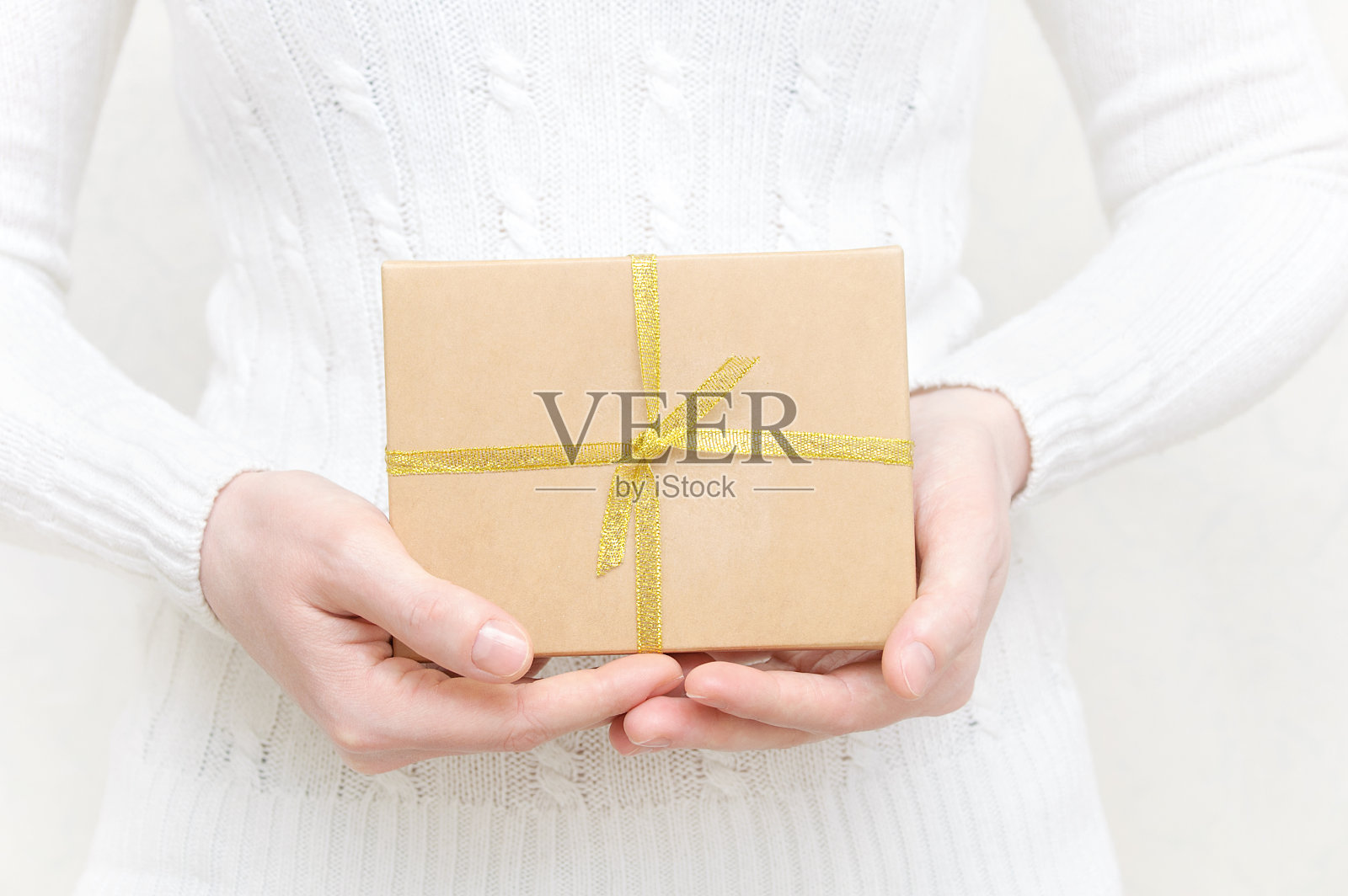 穿白色毛衣的女孩拿着一个装着礼物的盒子。照片摄影图片