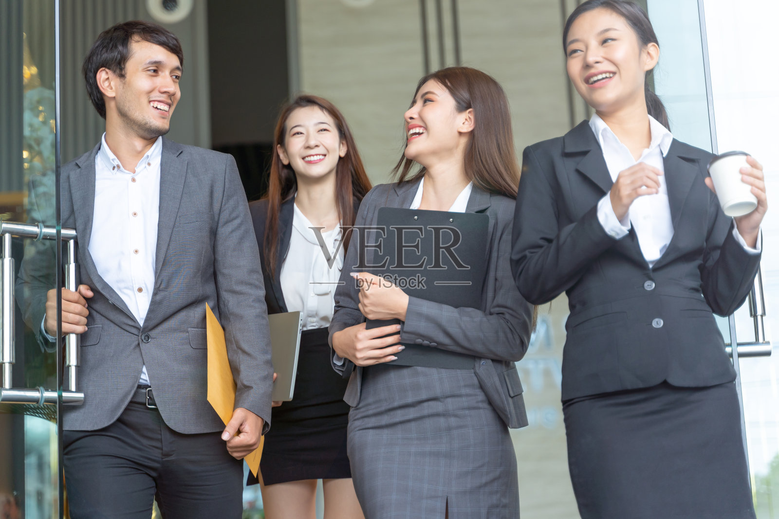 亚洲商务人士步行走出办公楼。年轻的商人和女商人在聊天，打开办公室的门。照片摄影图片