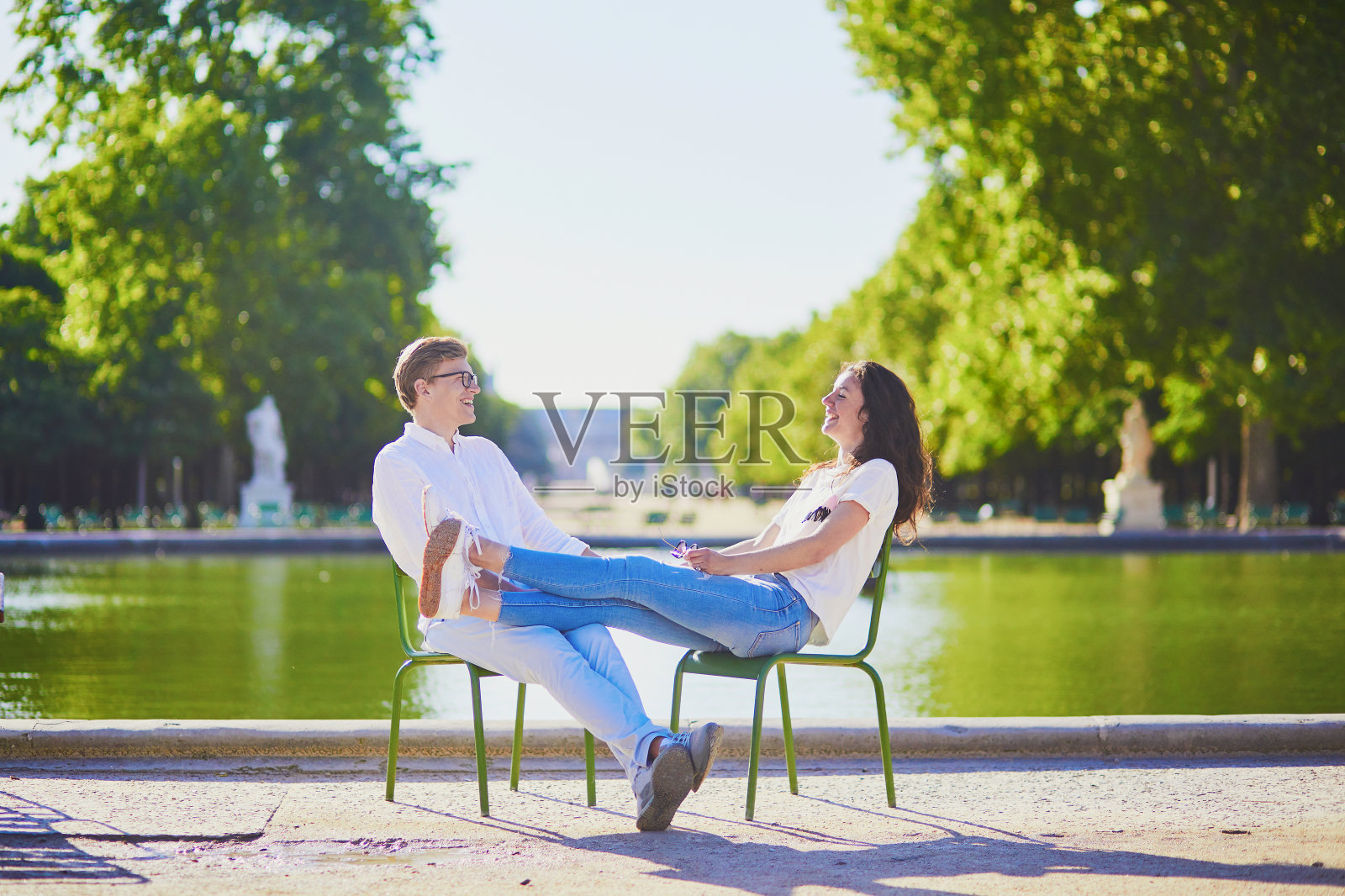 一对幸福浪漫的巴黎情侣，坐在杜乐丽花园的传统绿色金属椅子上照片摄影图片