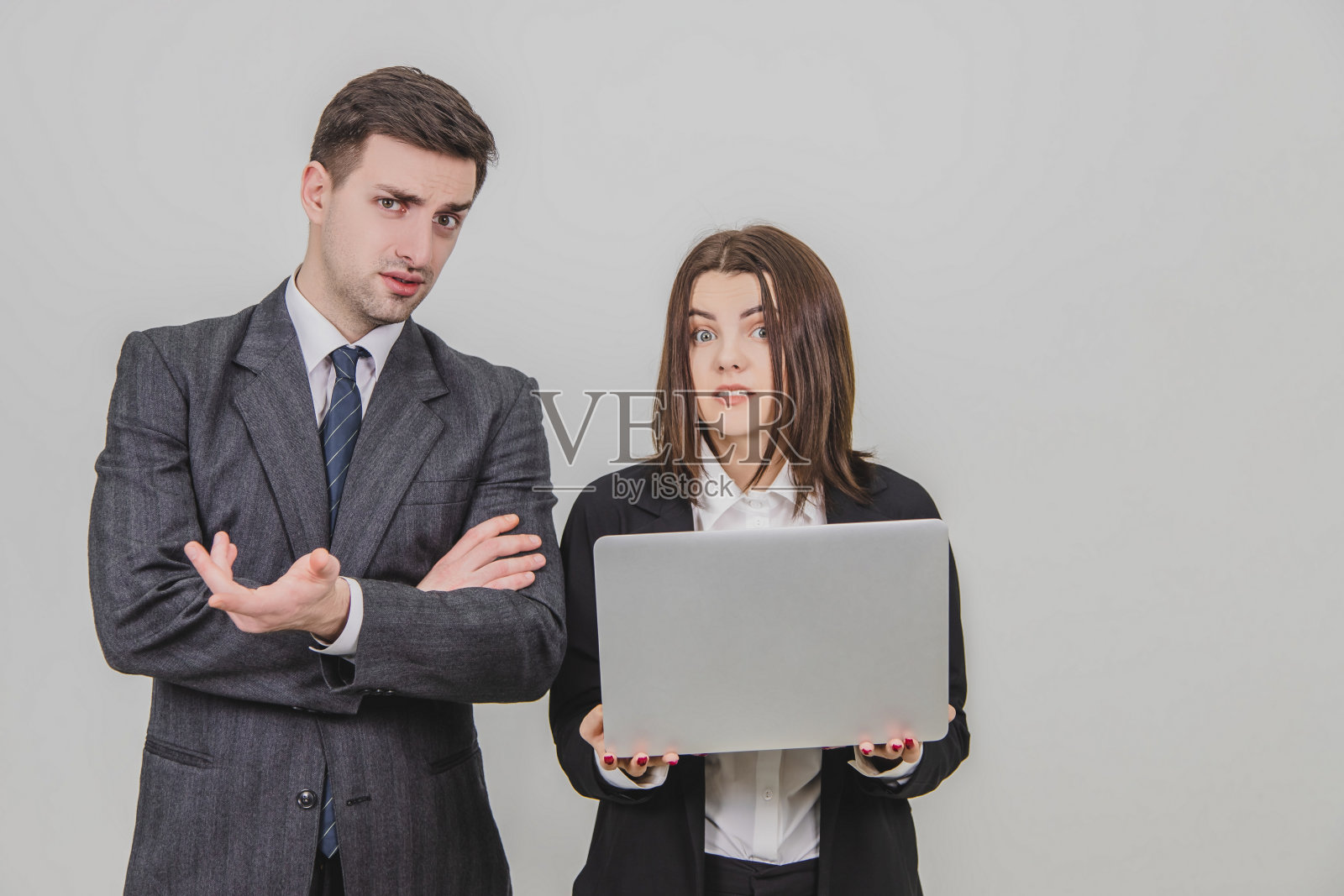 商业伙伴站着，在笔记本电脑里检查数据，看着摄像头，脸上露出困惑的表情。照片摄影图片