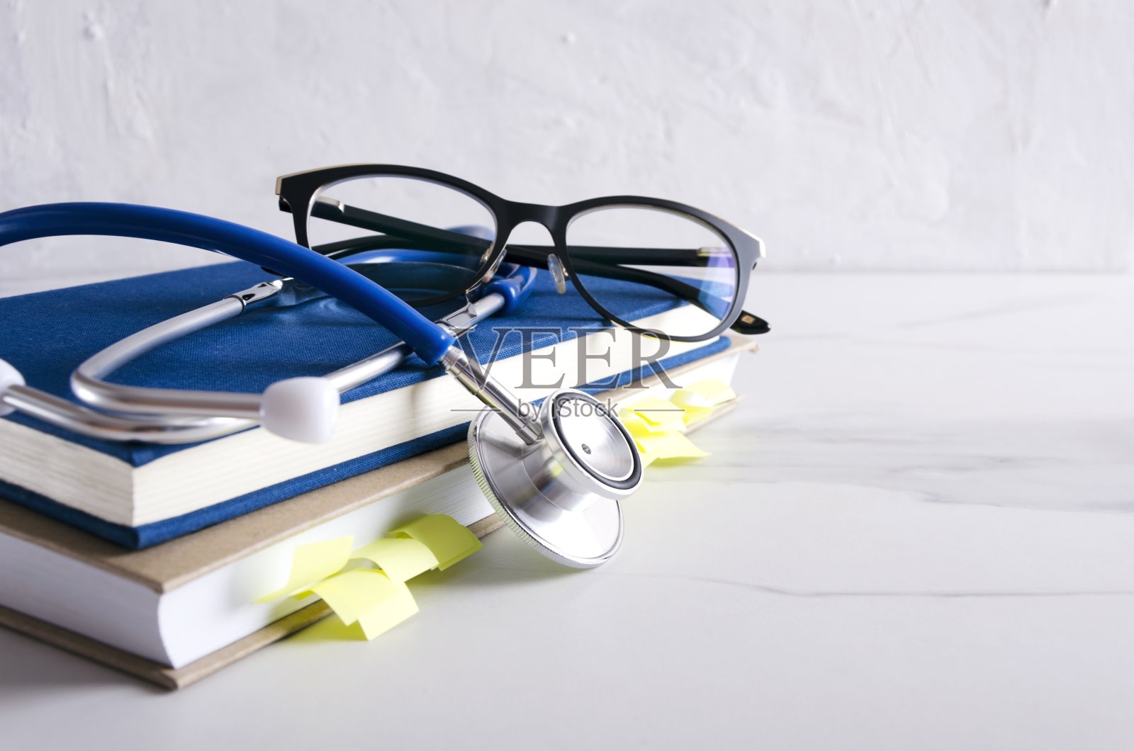 白色的桌子上放着眼镜、医学书籍和专业听诊器照片摄影图片