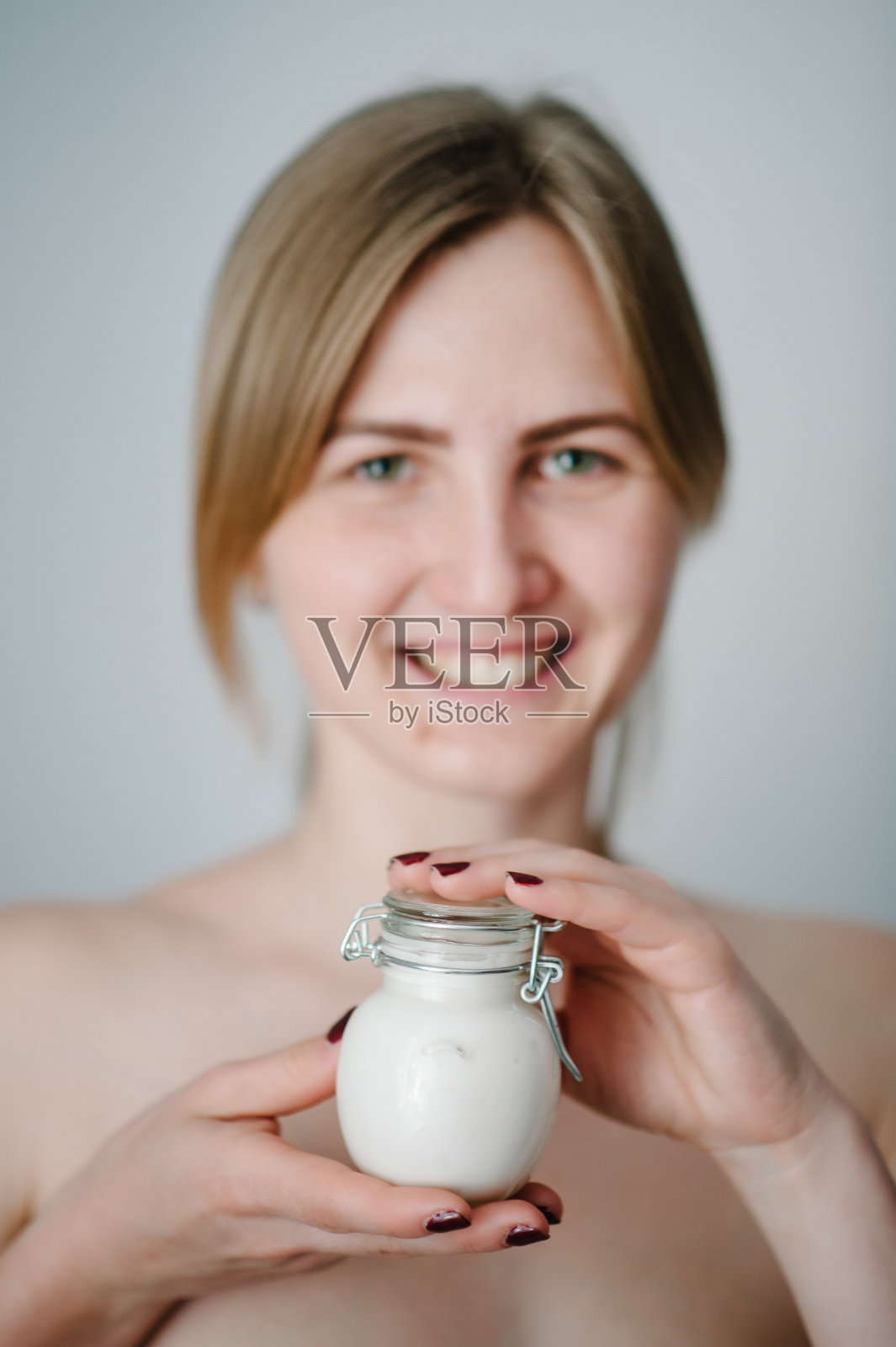 年轻女孩的照片与无瑕的皮肤。微笑的女人拿着一个小瓶的护肤霜和使用乳液，天然化妆品。美容、美容和水疗。健康。特写，选择焦点。照片摄影图片