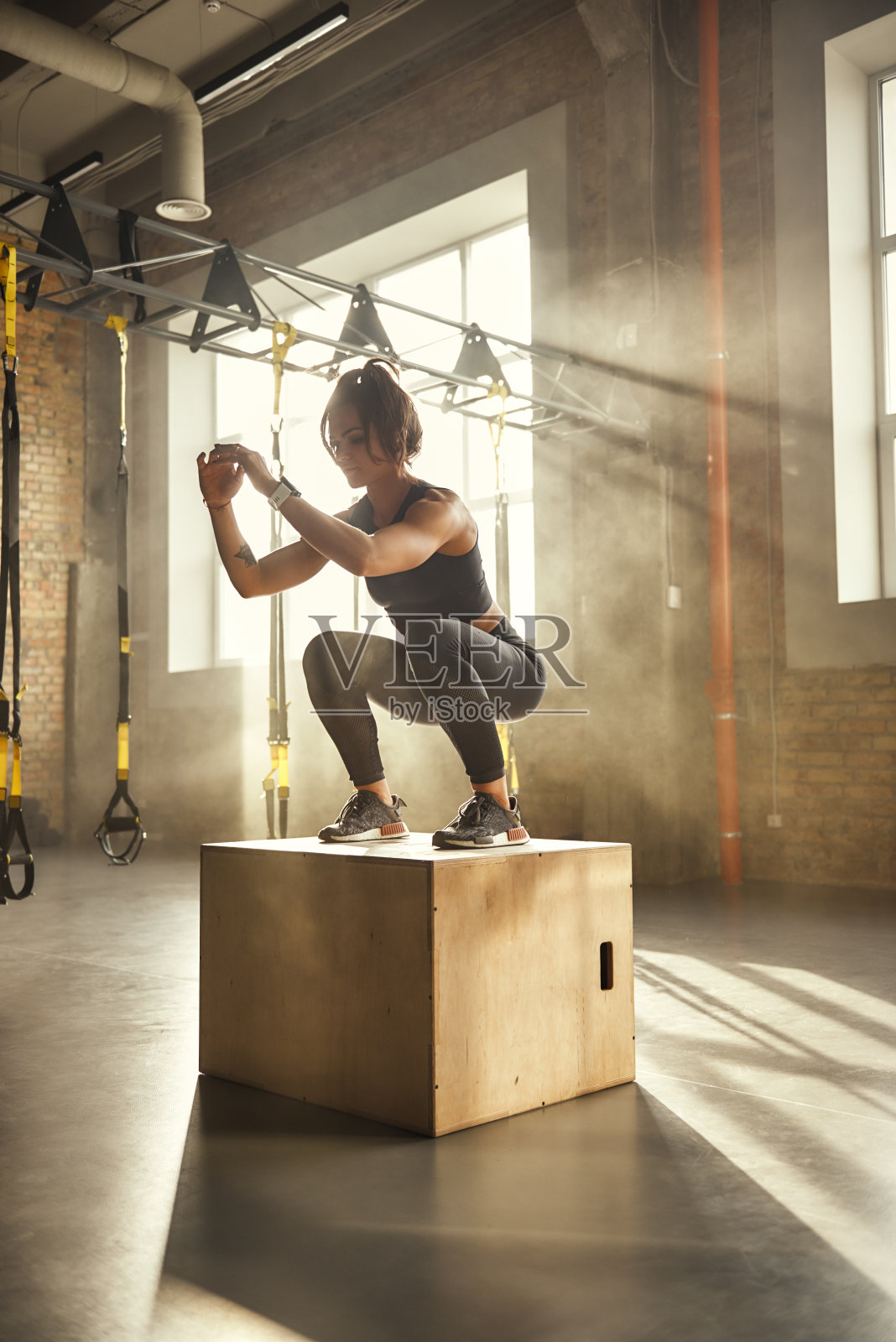挑战自己。侧视图的运动员妇女在运动服装做蹲，而站在木箱在健身房照片摄影图片