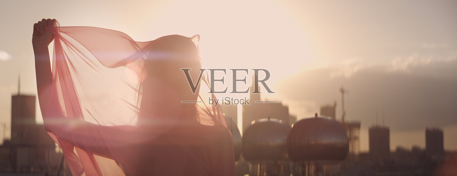 屋顶日落。妩媚的女人在优雅的服装玩丝质围巾照片摄影图片