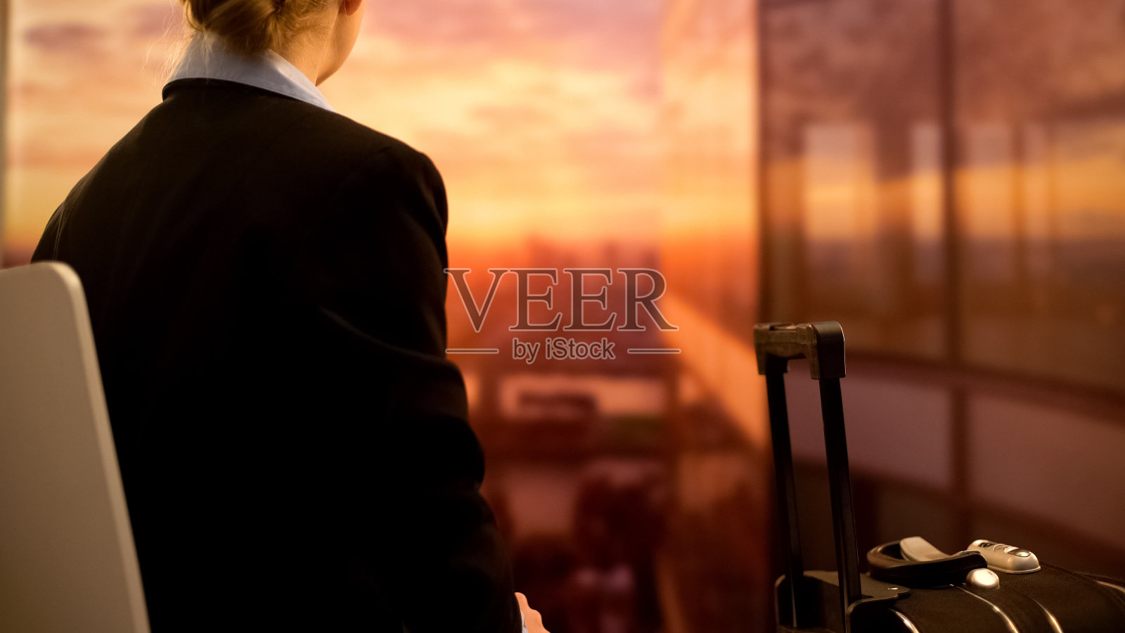 一个女人提着行李箱坐在机场欣赏美丽的日落，背景照片摄影图片