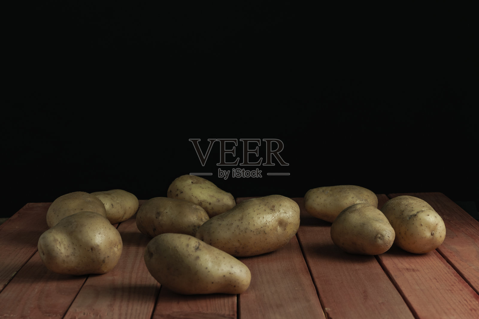 红色木桌上放着新鲜的土豆，背景是漂亮的黑色。照片摄影图片