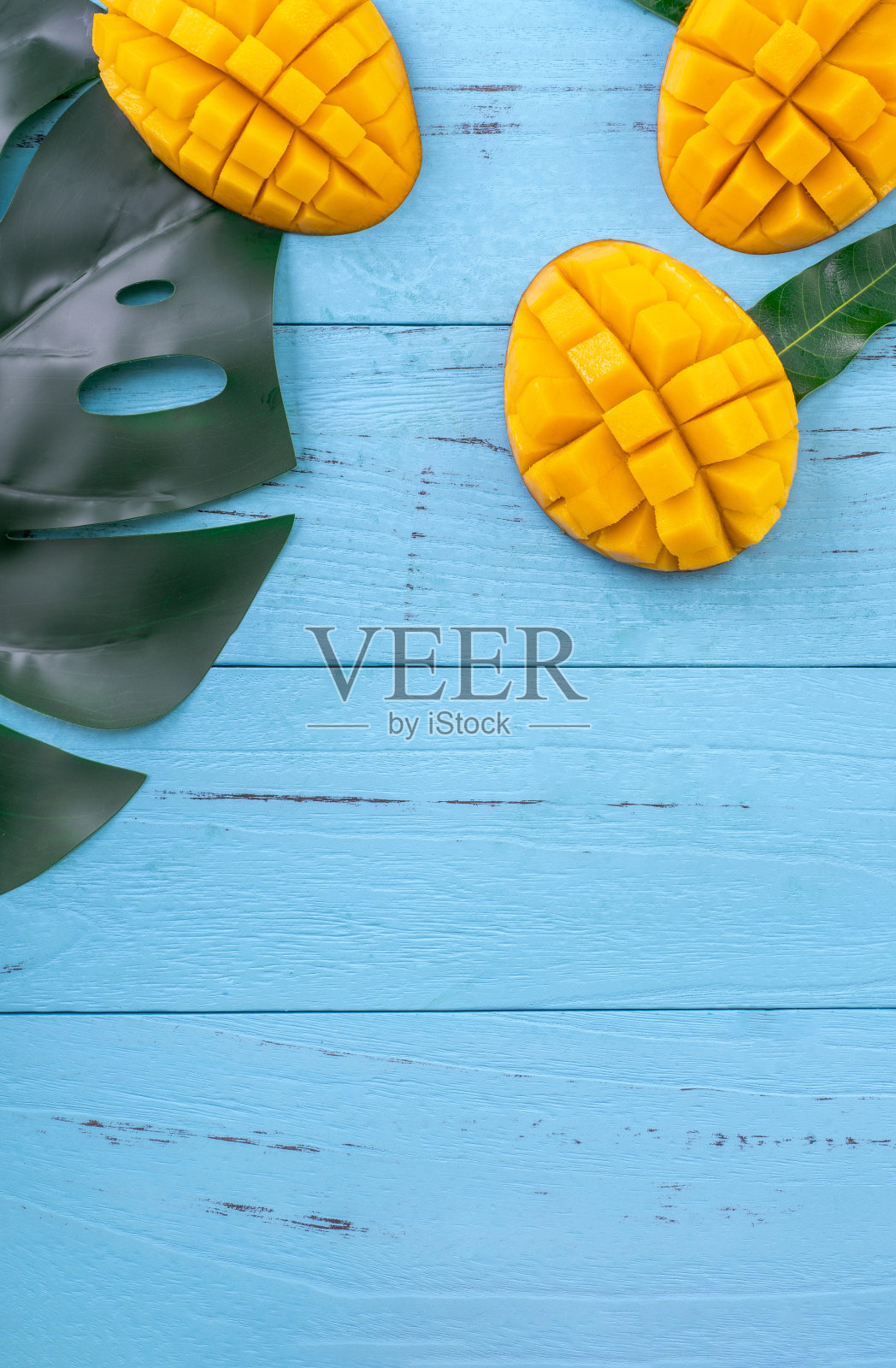 新鲜的芒果-美丽的切碎的水果，绿色的叶子在明亮的蓝色木材背景。热带水果设计理念。平的。前视图。本空间照片摄影图片