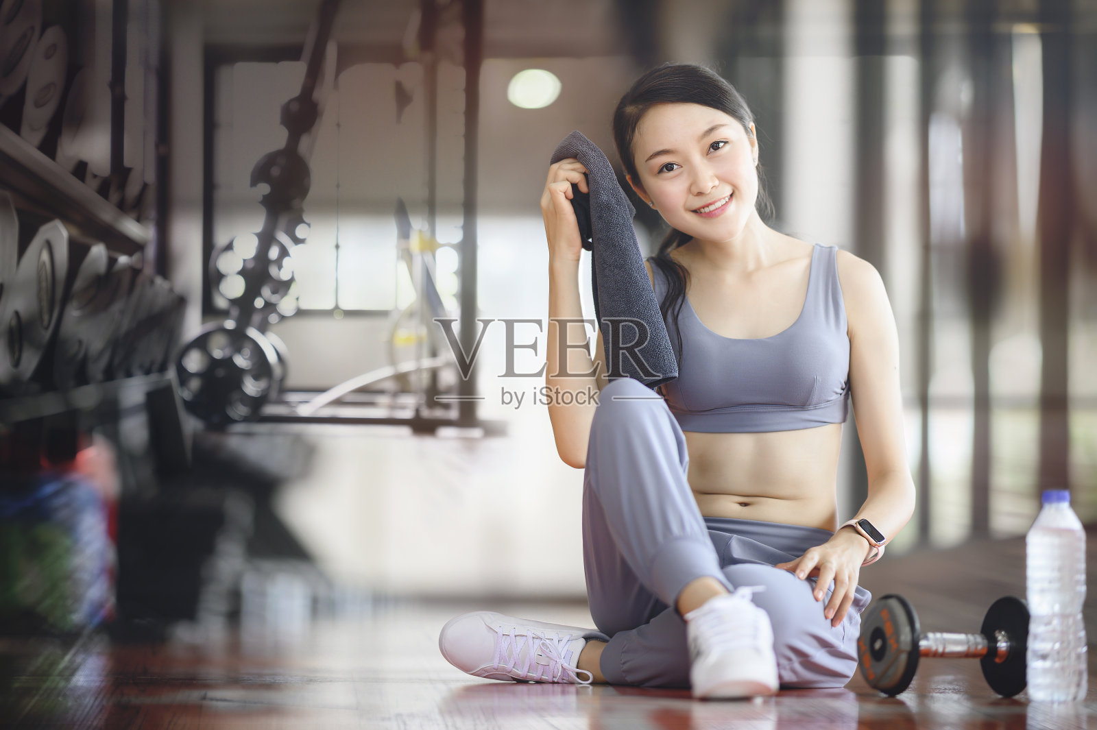 女人在健身房里锻炼，拿着毛巾，微笑着看着镜头，放松照片摄影图片