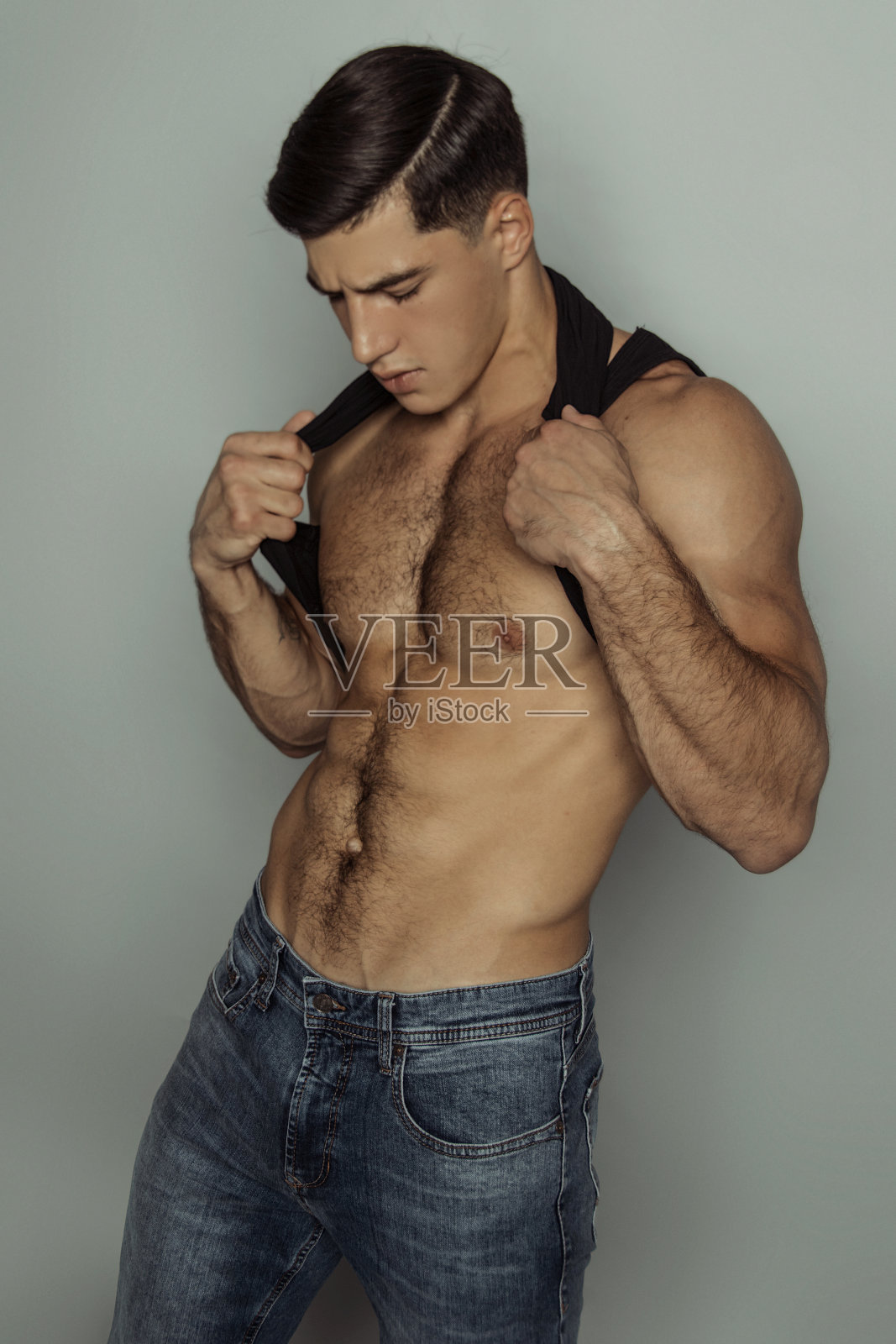 肌肉强壮美丽的剥离男性模特在牛仔蓝色牛仔裤和黑色t恤灰色孤立的字体背景照片摄影图片