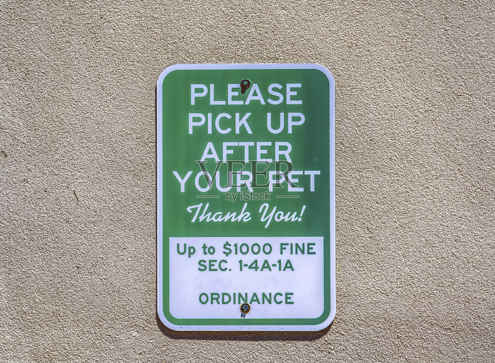 标牌上写着“请捡起你的宠物”，贴在混凝土墙上照片摄影图片