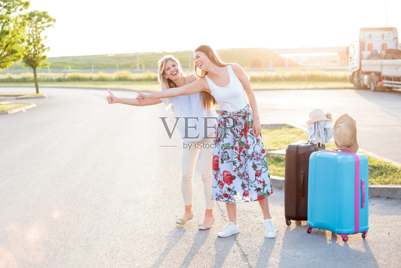 两个快乐的年轻女人有一个伟大的时间搭便车在路边照片摄影图片