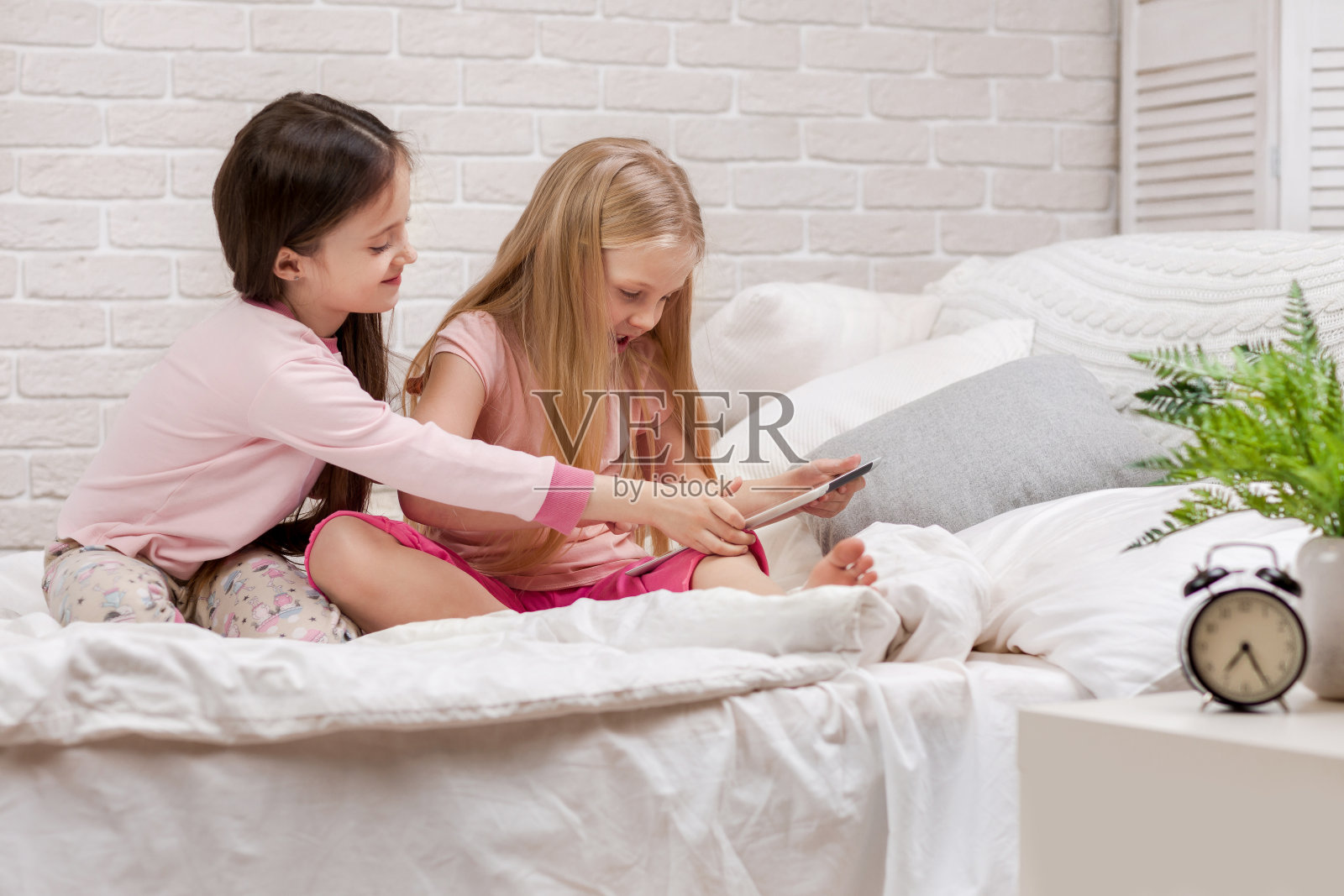 两个可爱的小女孩在床上使用电子平板电脑。照片摄影图片