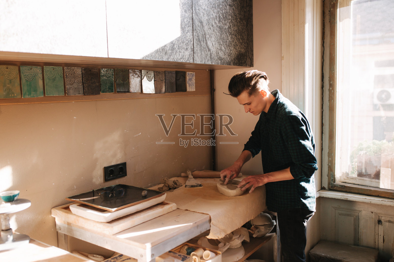 男陶工正在寻找一件制品。年轻的陶工在他的作坊里。英俊的男人工作照片摄影图片