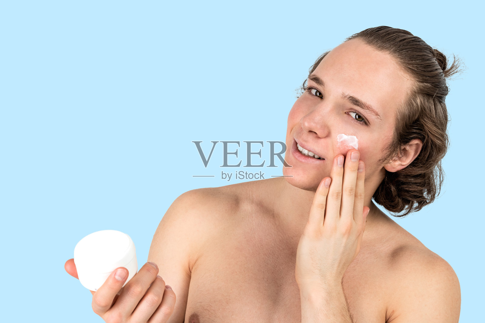 英俊的年轻赤膊男子在他的脸上涂抹霜在白色的背景孤立。男性健康和皮肤护理照片摄影图片